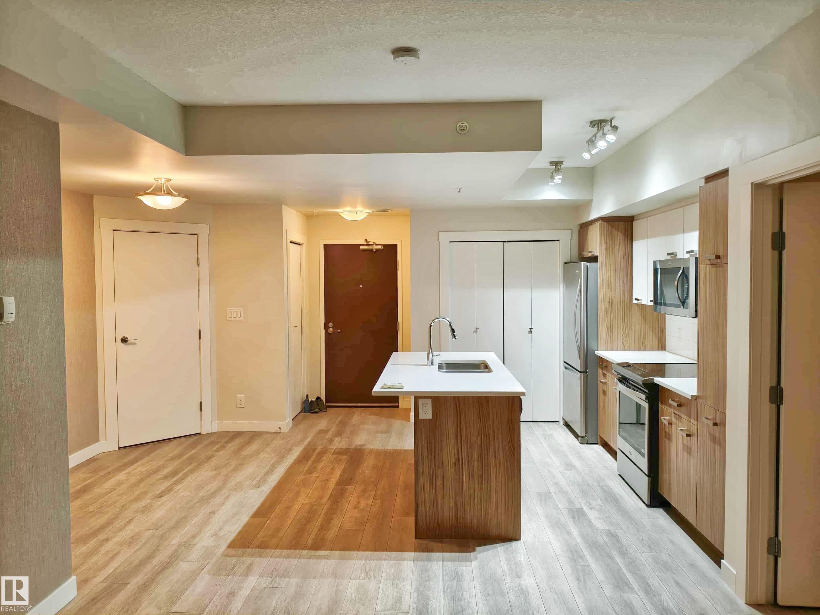 Kitchen featuring a center island with sink, stainless steel appliances, wood-finish cabinetry, and light countertops - #2505 10410 102 Av Nw, Edmonton, AB - Indoor Photo Showing Kitchen With Double Sink