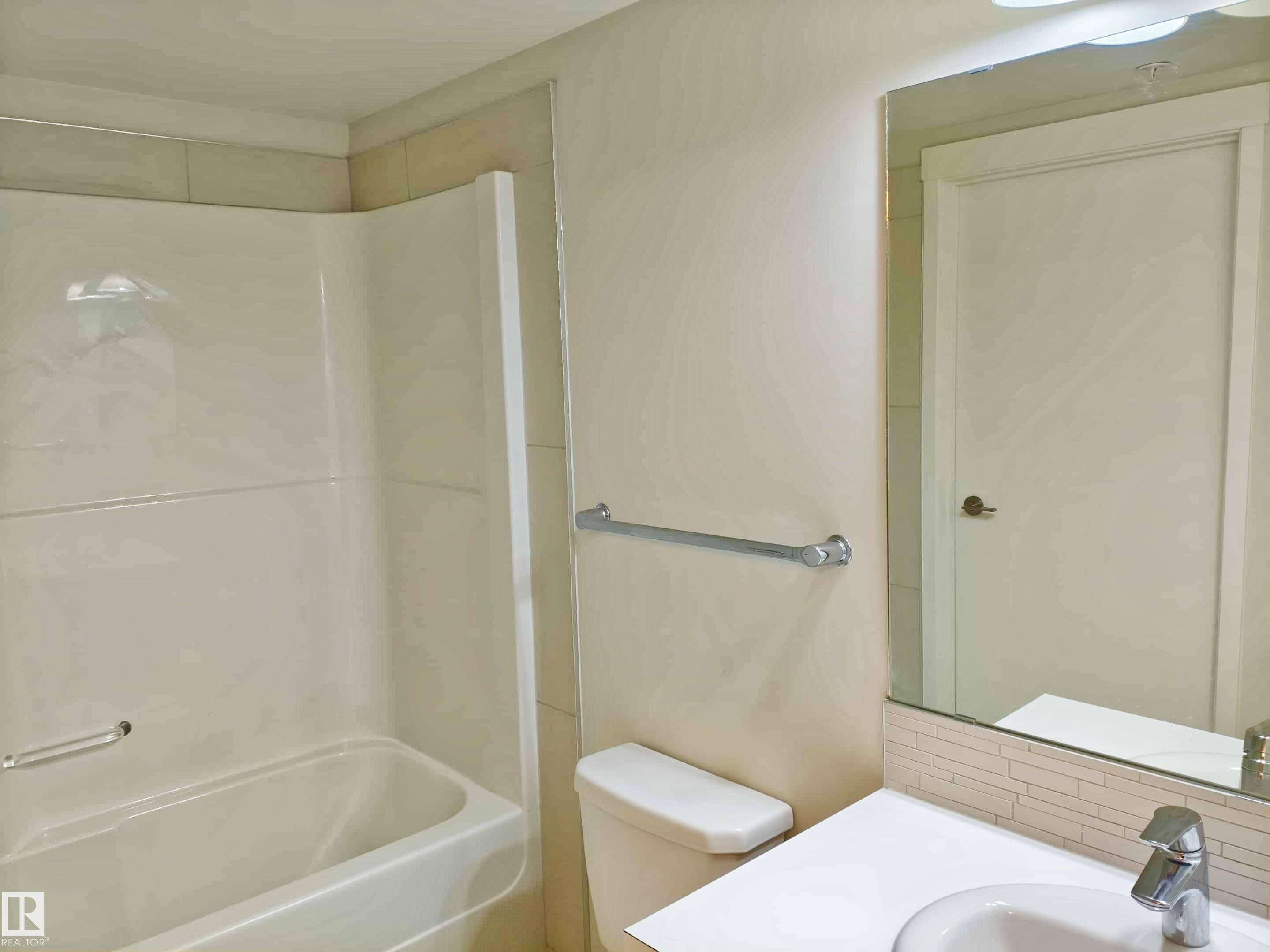 Bathroom featuring a white bathtub with a shower surround, a white toilet, and a vanity with a drop-in sink and chrome faucet - #2505 10410 102 Av Nw, Edmonton, AB - Indoor Photo Showing Bathroom