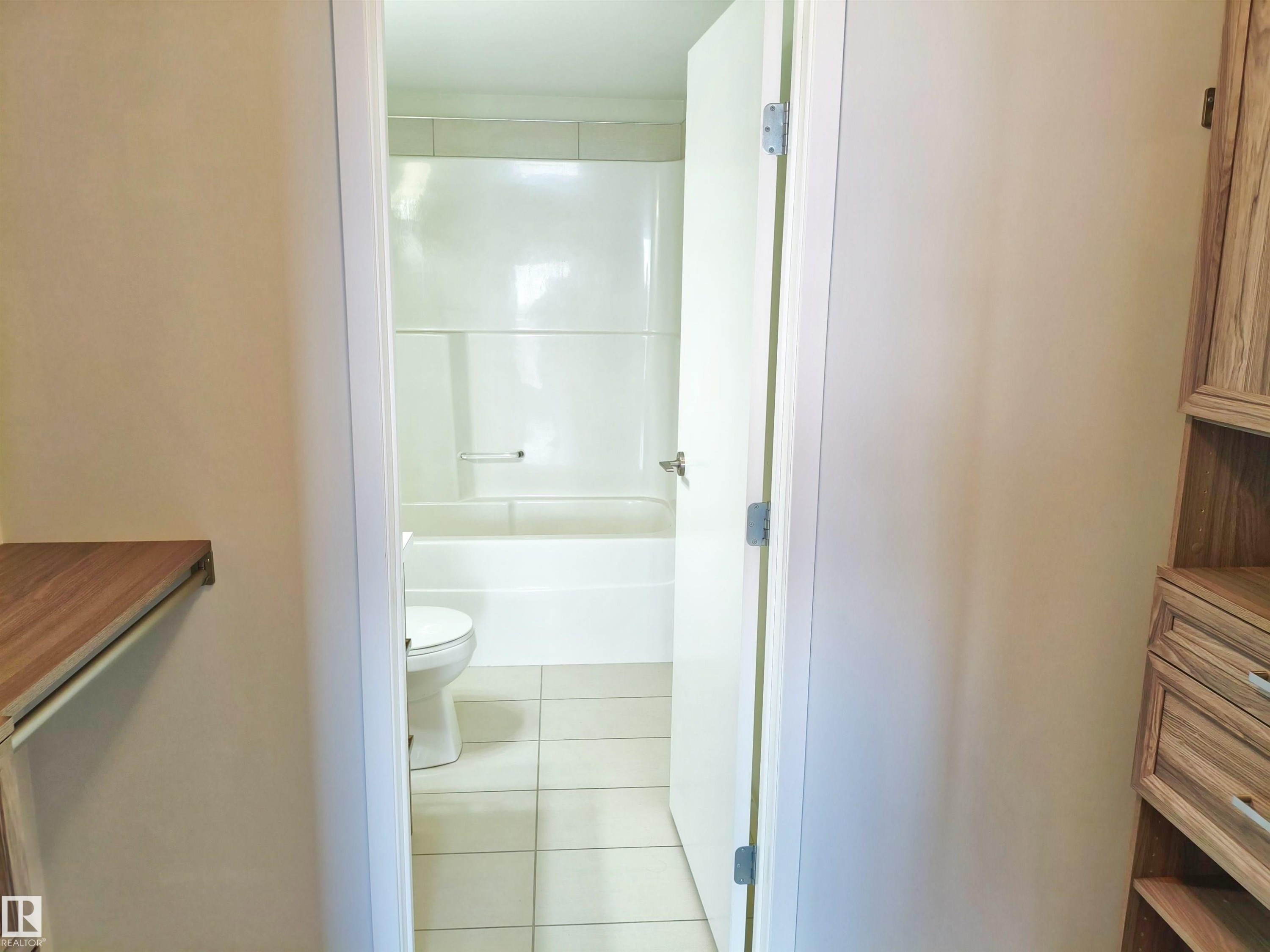 Bathroom featuring a white bathtub and shower surround, white toilet, and light-toned tile flooring - #2505 10410 102 Av Nw, Edmonton, AB - Indoor Photo Showing Bathroom