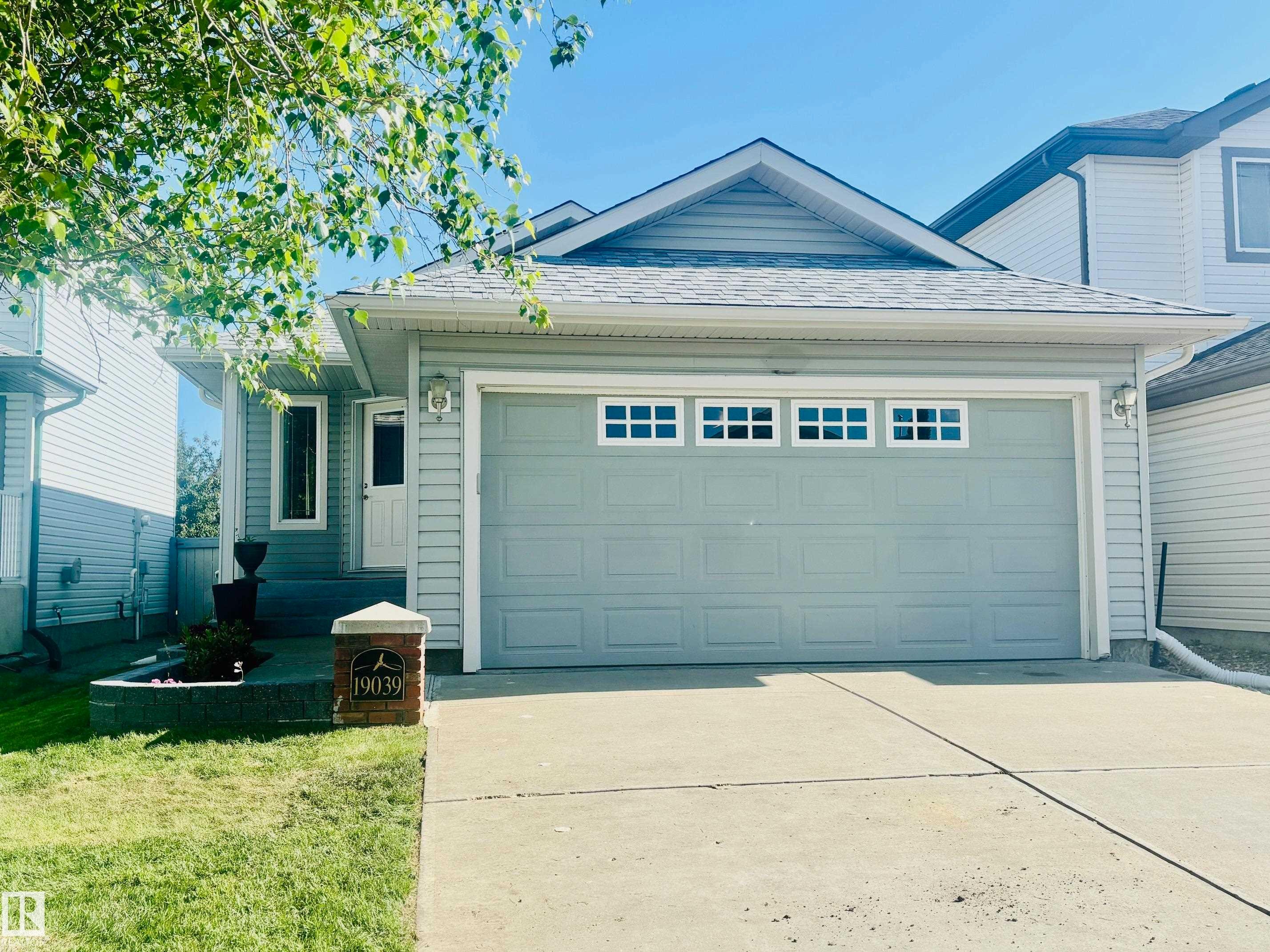 Light blue siding exterior with a contrasting gray garage door featuring decorative windows - 19039 47 Avenue Nw, Edmonton, AB - Outdoor