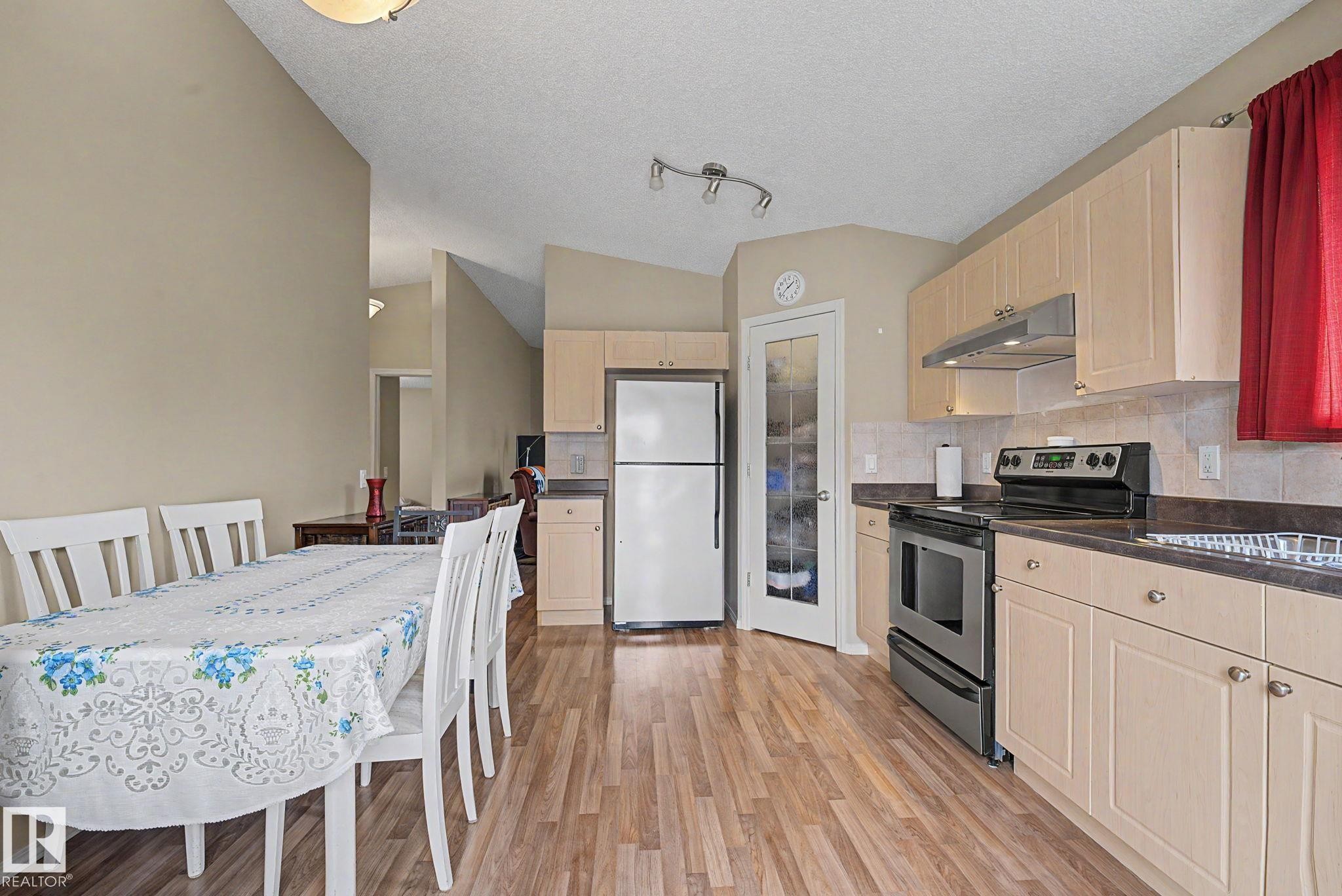 Kitchen and dining area featuring wood-finish flooring, light-toned cabinetry, stainless steel range, and a frosted glass pantry door - 19039 47 Avenue Nw, Edmonton, AB - Indoor