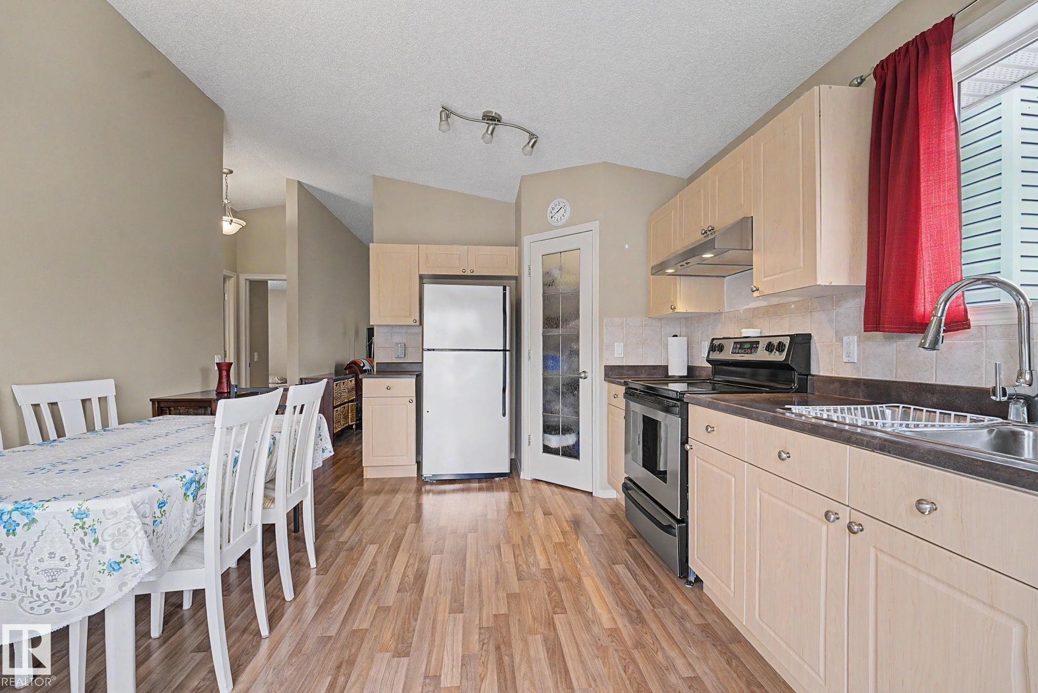 Kitchen featuring wood-finish flooring, light-toned cabinetry, stainless steel appliances, and a glass-paneled pantry door - 19039 47 Avenue Nw, Edmonton, AB - Indoor Photo Showing Kitchen
