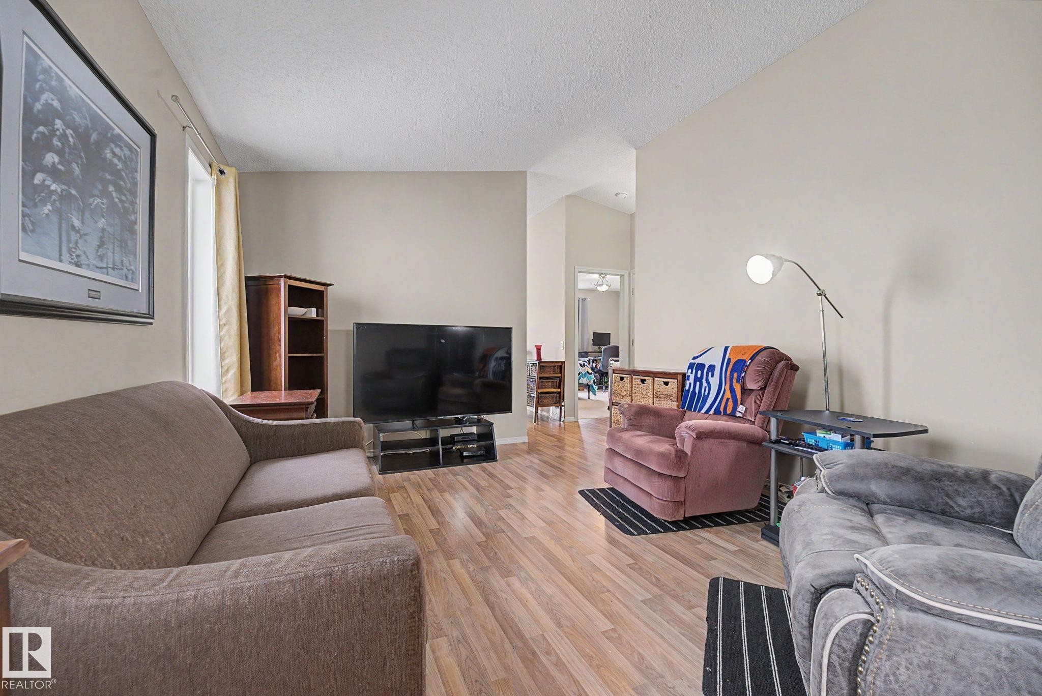 Spacious living area featuring wood-finish flooring, neutral wall tones, and vaulted ceilings - 19039 47 Avenue Nw, Edmonton, AB - Indoor Photo Showing Living Room