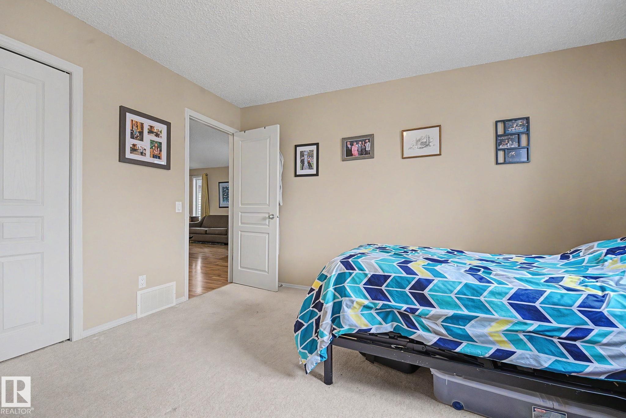 Neutral-toned walls and plush carpeting characterize this room, featuring a white paneled door and an open doorway revealing wood-finish flooring beyond - 19039 47 Avenue Nw, Edmonton, AB - Indoor Photo Showing Bedroom