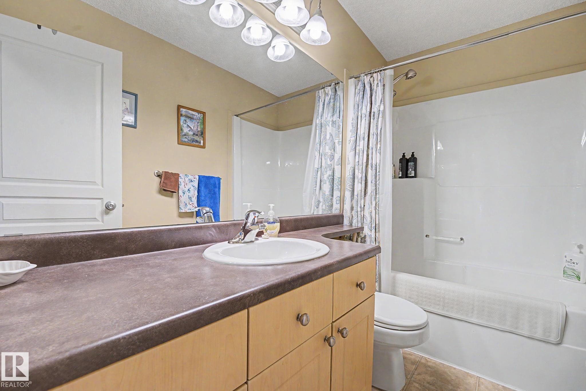 Bathroom featuring a light wood-finish vanity with a dark countertop, white drop-in sink, and chrome faucet - 19039 47 Avenue Nw, Edmonton, AB - Indoor Photo Showing Bathroom