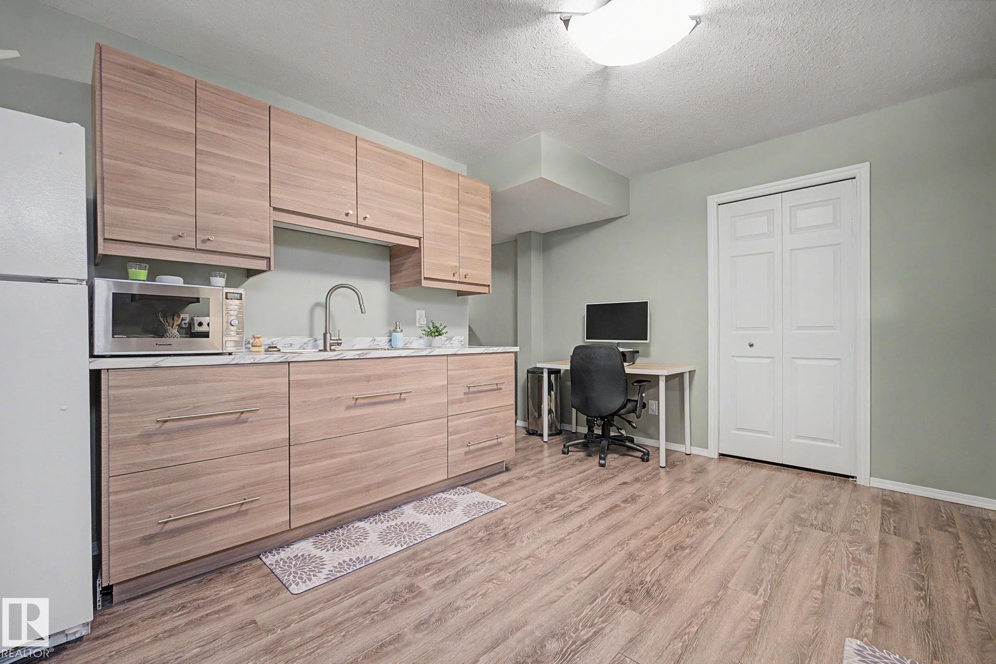 Compact kitchen area featuring wood-finish cabinetry, a white countertop, and a stainless steel sink with a gooseneck faucet - 19039 47 Avenue Nw, Edmonton, AB - Indoor Photo Showing Kitchen