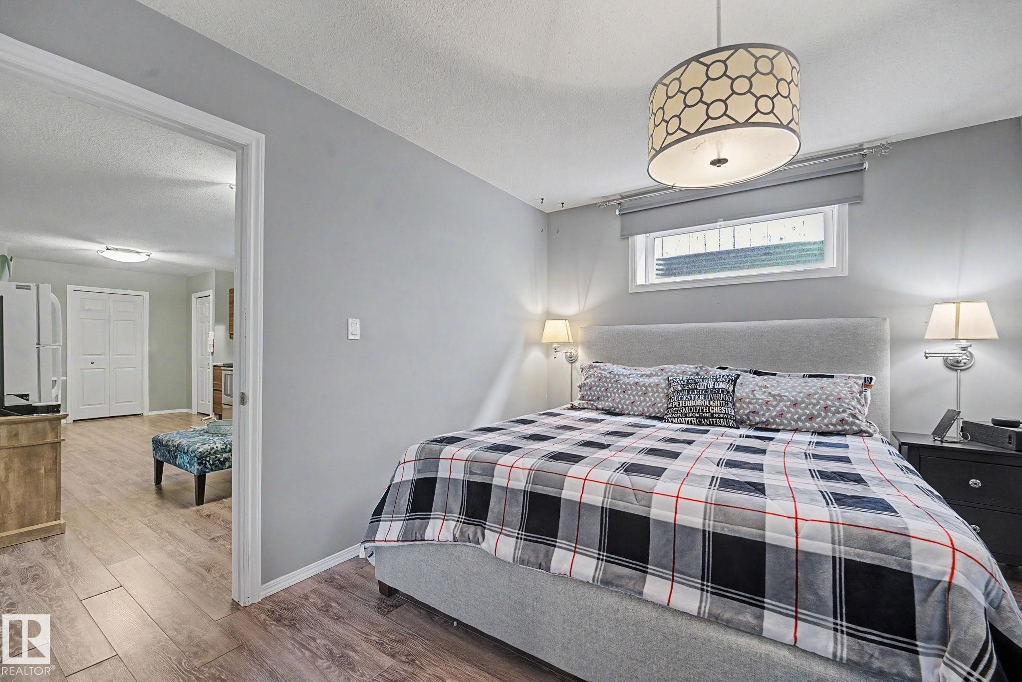 Light gray walls featuring a geometric drum pendant light fixture and a horizontal window with a roller shade - 19039 47 Avenue Nw, Edmonton, AB - Indoor Photo Showing Bedroom