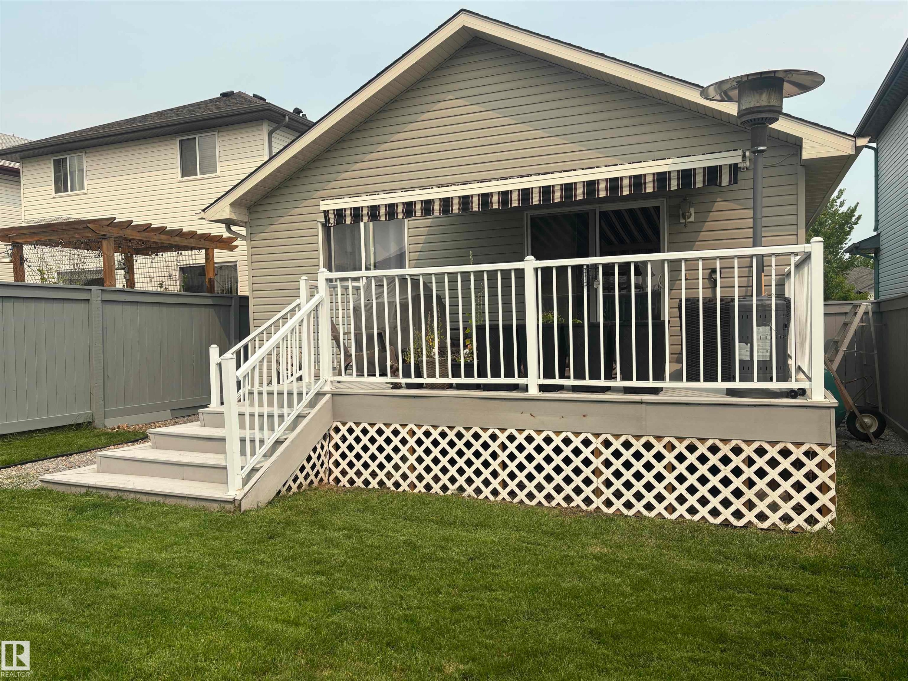 Exterior deck with white railing, striped retractable awning, and lattice skirting - 19039 47 Avenue Nw, Edmonton, AB - Outdoor With Deck Patio Veranda With Exterior