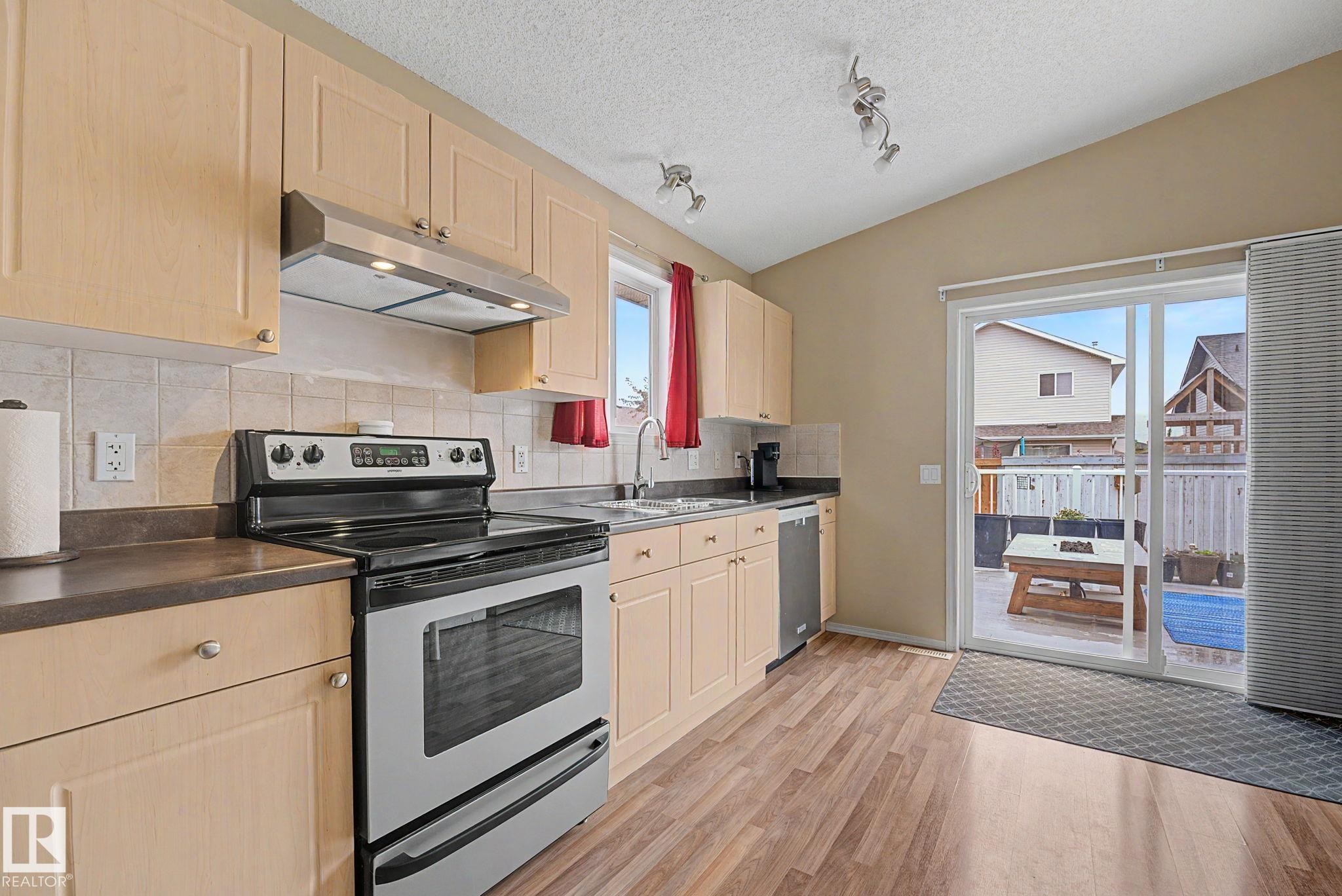 Kitchen featuring light wood-finish cabinetry, stainless steel appliances, and a tiled backsplash - 19039 47 Avenue Nw, Edmonton, AB - Indoor Photo Showing Kitchen