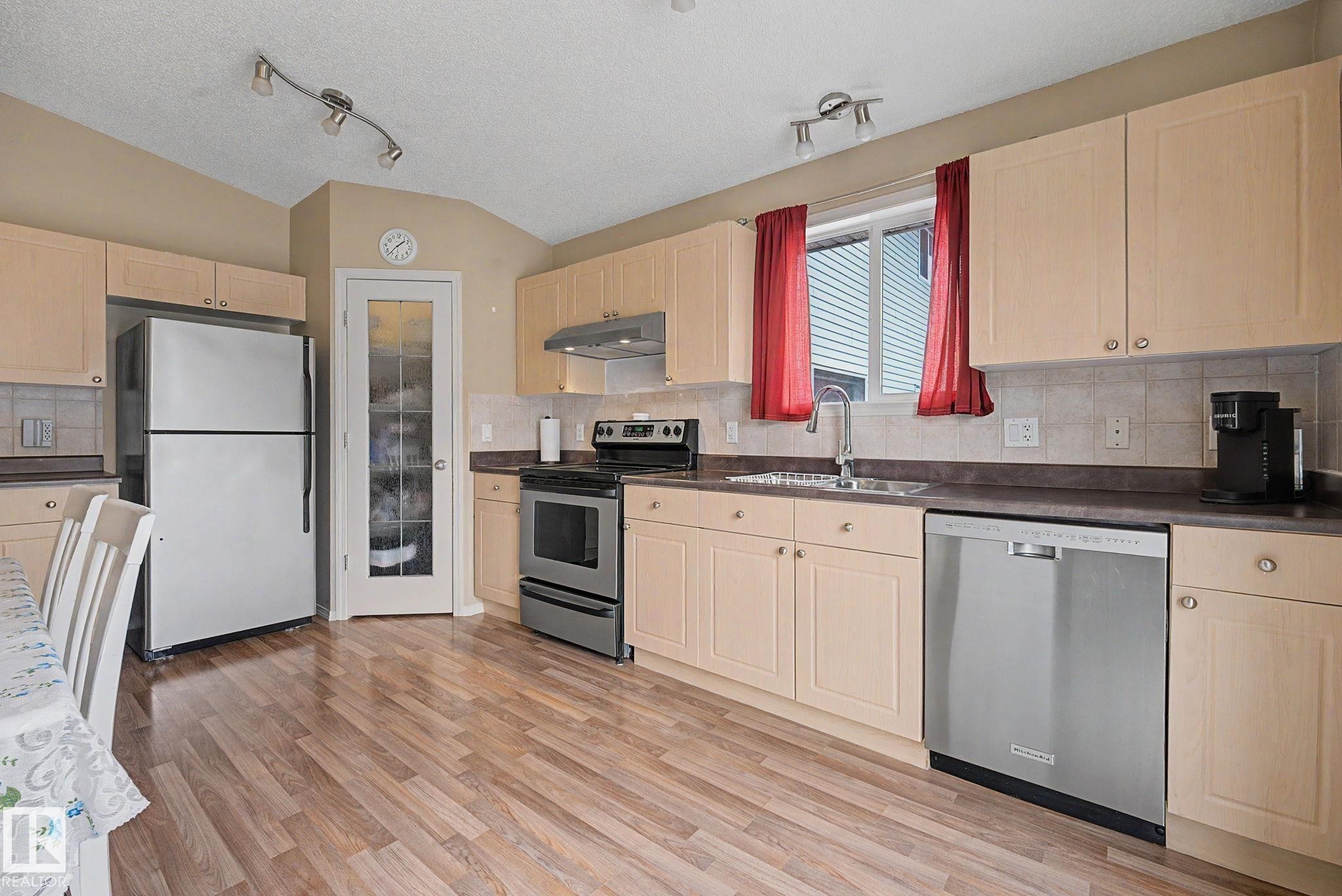 Kitchen featuring wood-finish flooring, light-toned cabinetry, stainless steel appliances, and track lighting - 19039 47 Avenue Nw, Edmonton, AB - Indoor Photo Showing Kitchen