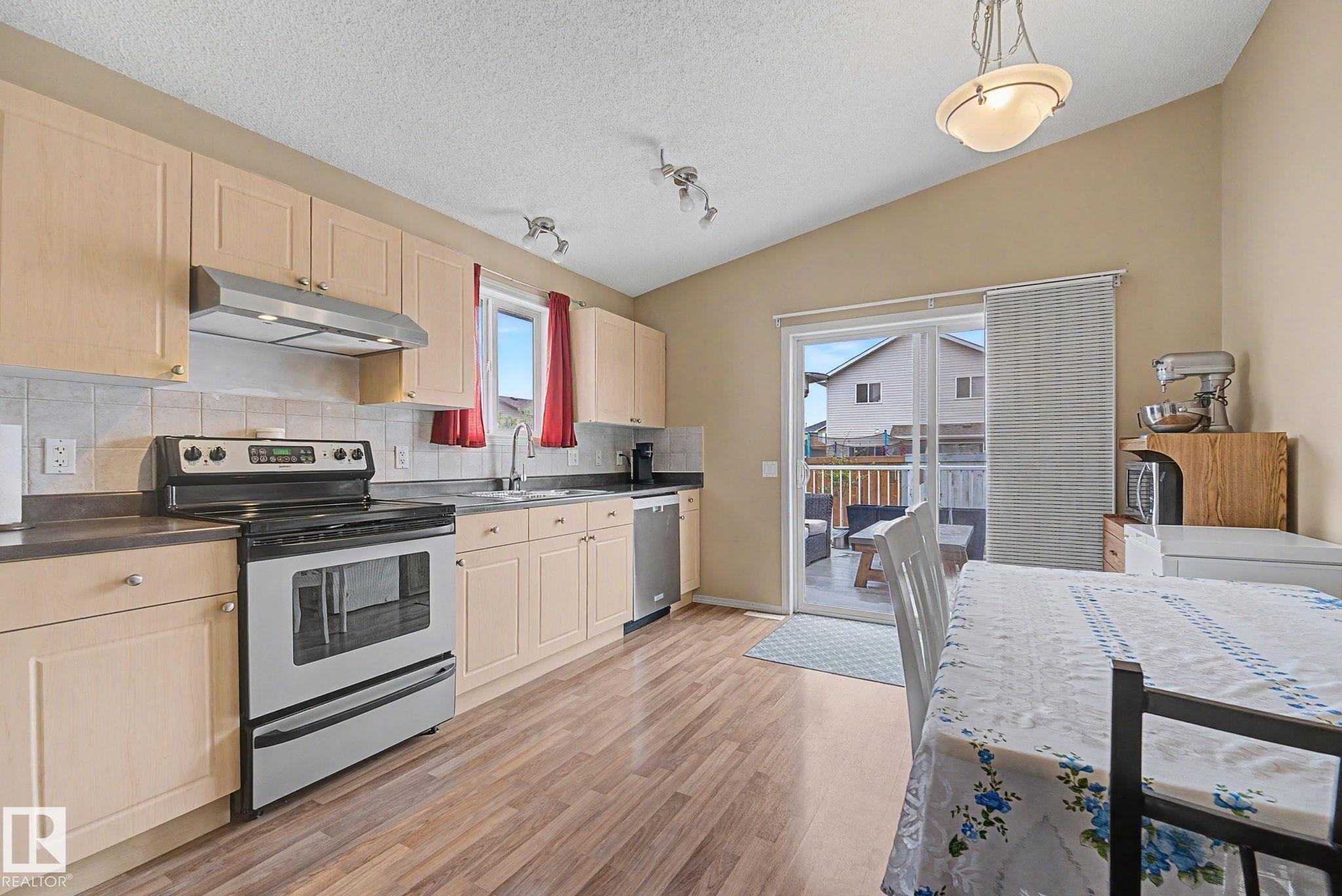 Kitchen featuring light wood-finish cabinetry, stainless steel appliances, and wood-finish flooring - 19039 47 Avenue Nw, Edmonton, AB - Indoor