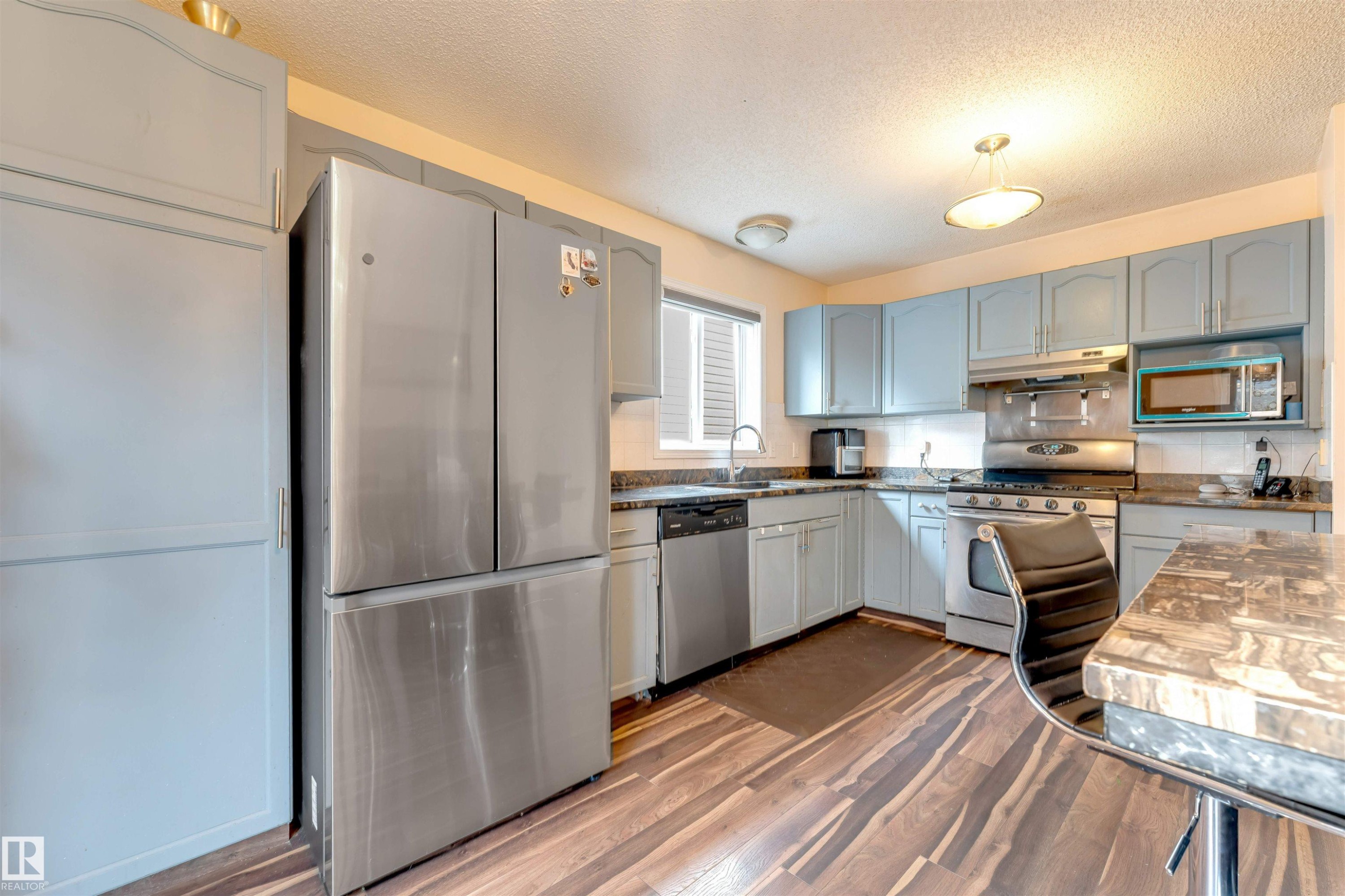 Kitchen featuring light blue cabinetry, stainless steel appliances, wood-finish flooring, and a window with blinds - 312 Beringer Crescent Nw, Edmonton, AB - Indoor Photo Showing Kitchen