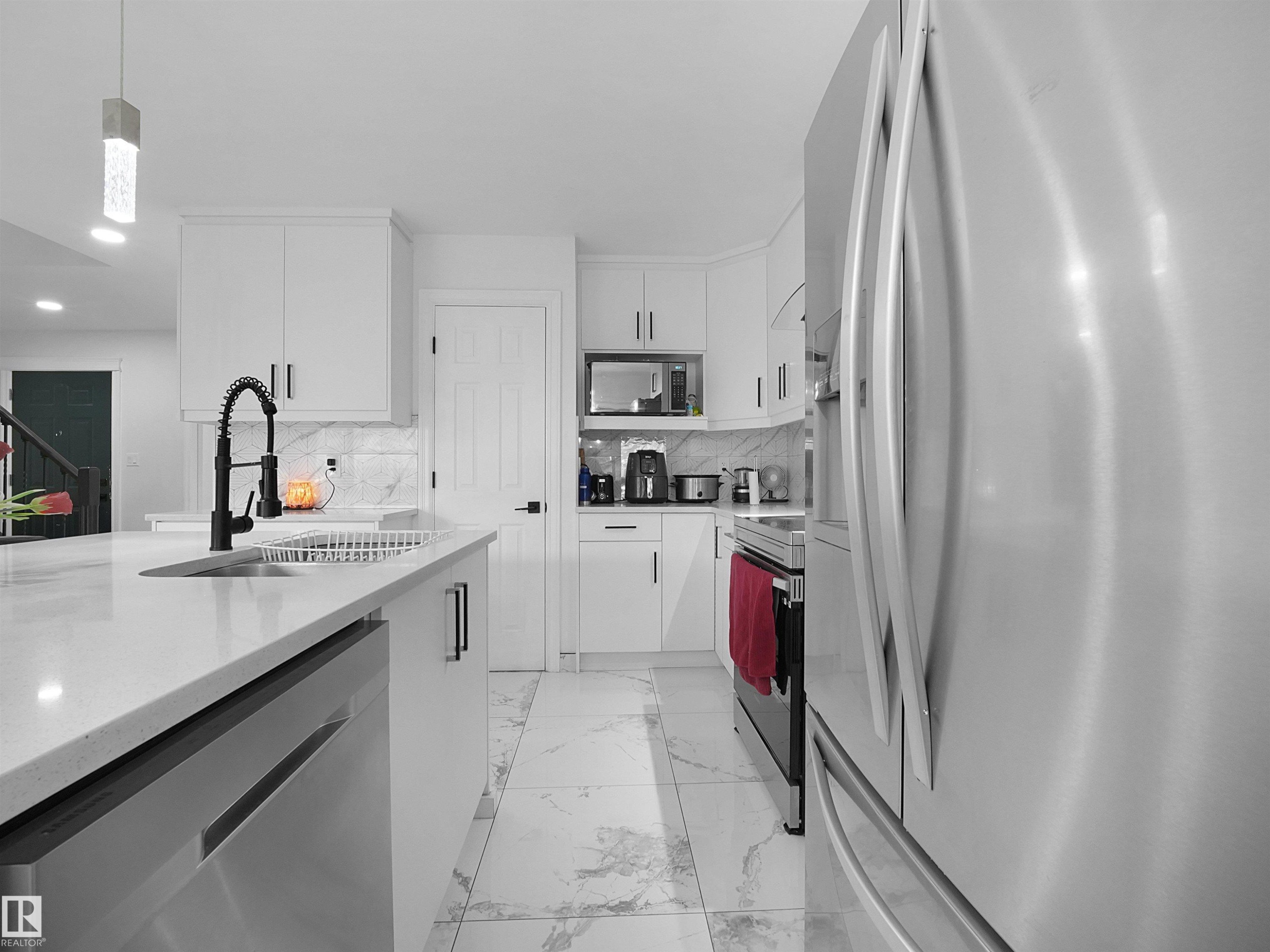 Modern kitchen featuring white cabinetry, a large center island with integrated sink and dishwasher, stainless steel appliances, and marble-look tile flooring - 2418 32B Street, Edmonton, AB