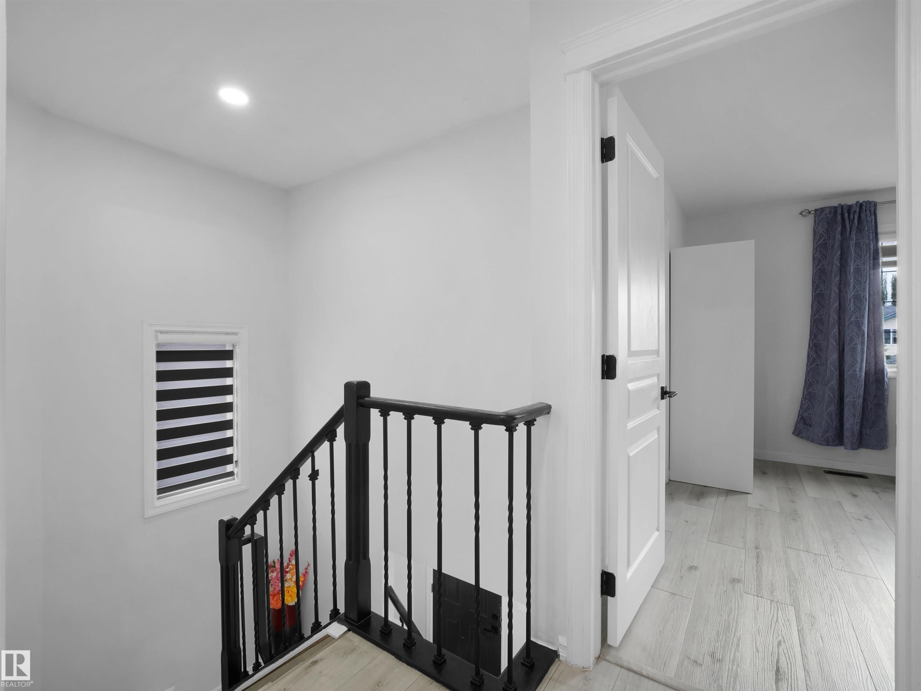 Hardwood-finish flooring extending from the hallway into an adjacent room, complemented by a white paneled door with matte black hardware - 2418 32B Street, Edmonton, AB