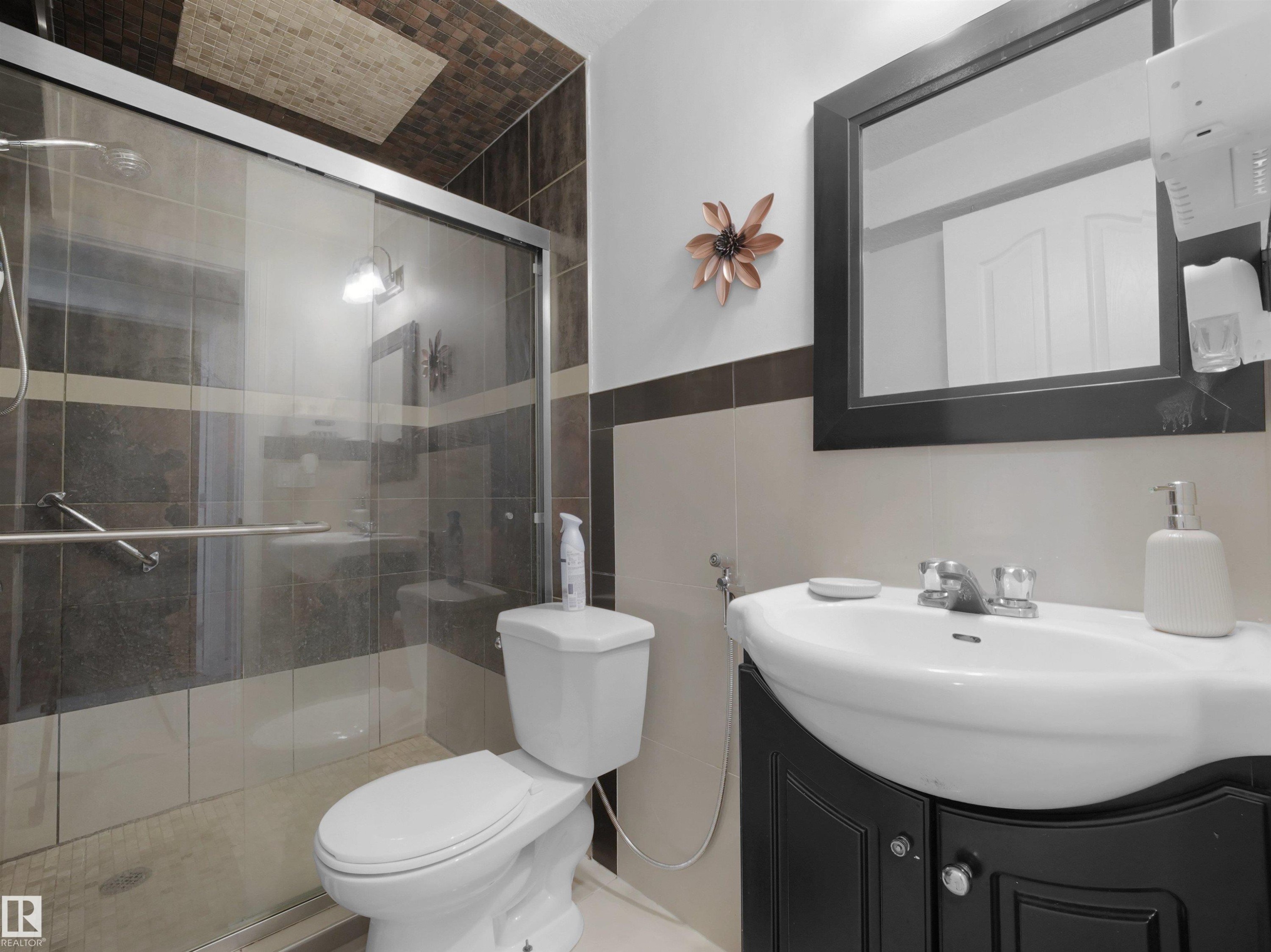 Bathroom featuring a glass-enclosed shower, a wall-mounted sink with dark wood-finish vanity, a framed mirror, and a mosaic-tiled ceiling accent - 2418 32B Street, Edmonton, AB