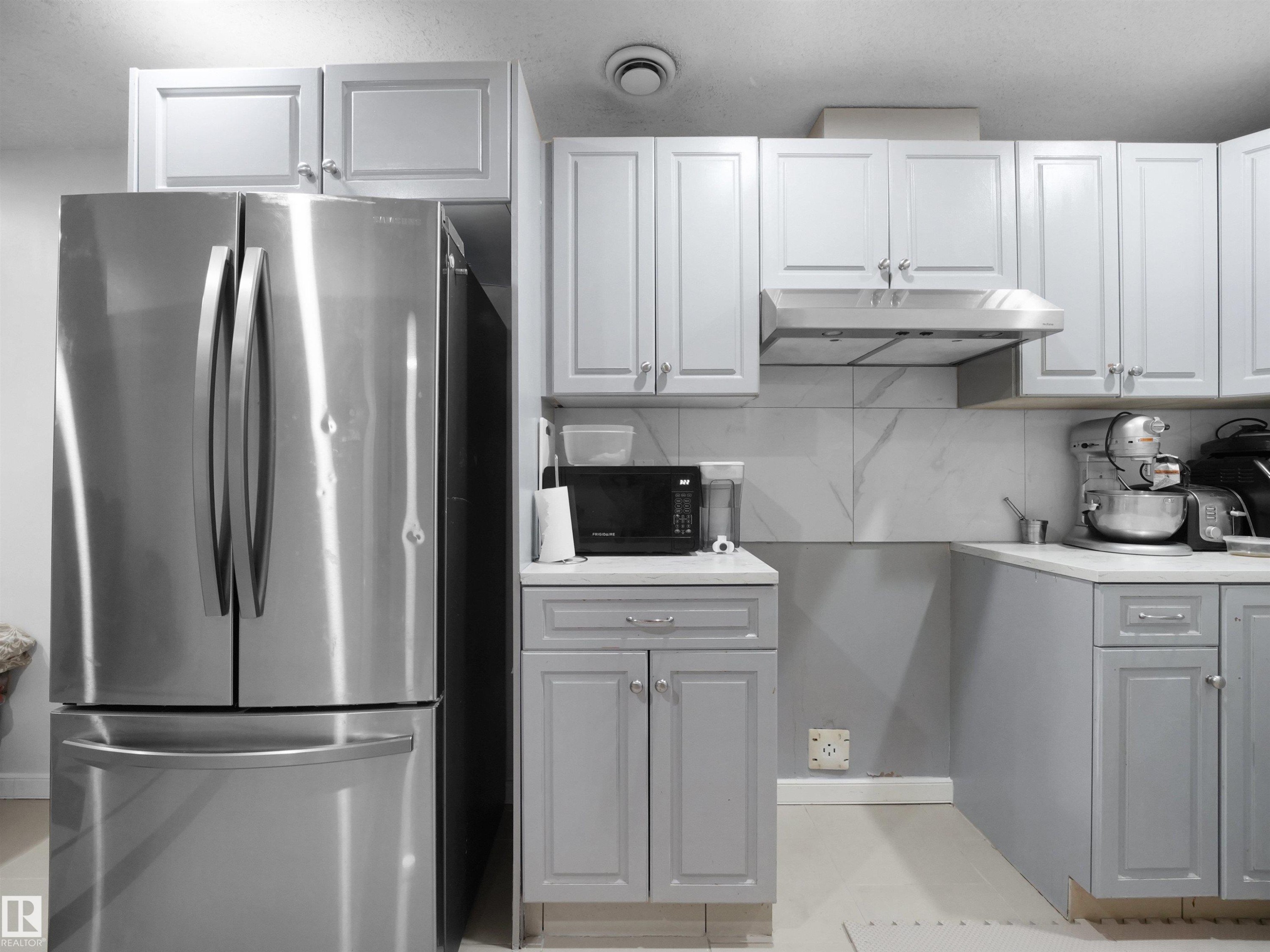 Kitchen featuring upper white cabinetry, lower gray cabinetry, stainless steel appliances, and a marble-patterned backsplash - 2418 32B Street, Edmonton, AB