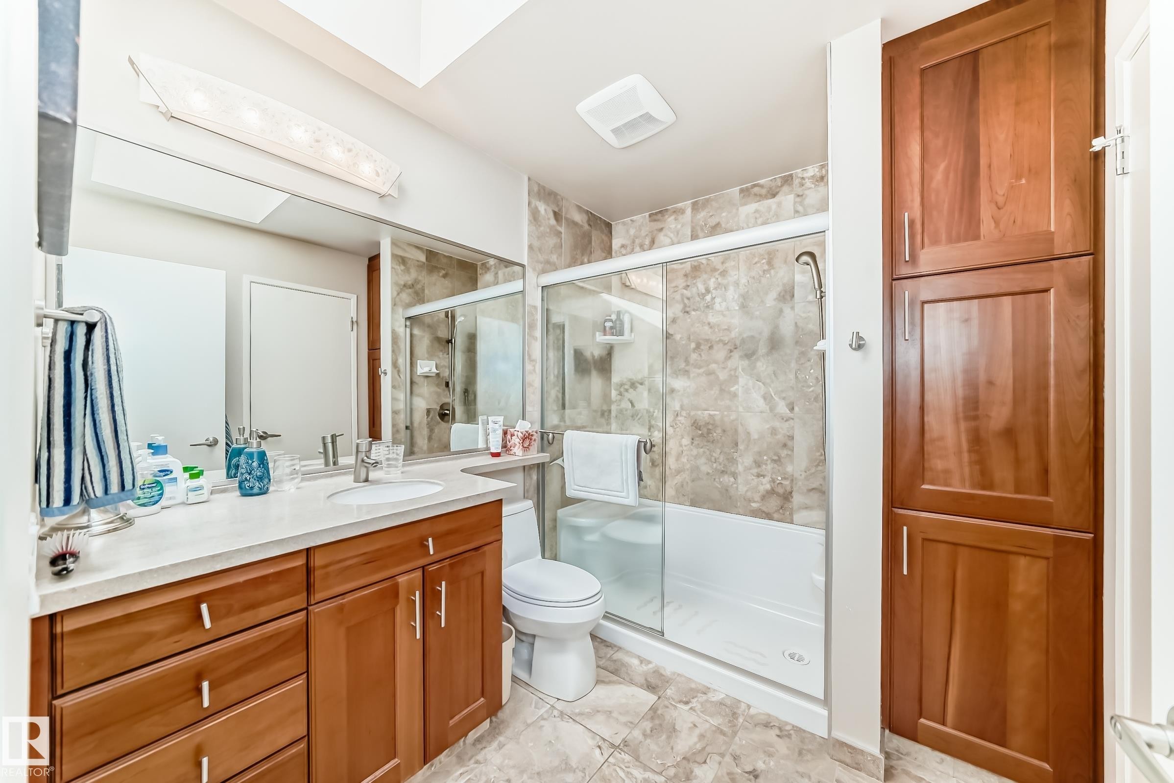 Bathroom featuring a vanity with a rectangular sink, a shower-tub combination with a sliding glass door, extensive wall and floor tiling, and built-in cabinetry - 7930 111 Street, Edmonton, AB - Indoor Photo Showing Bathroom