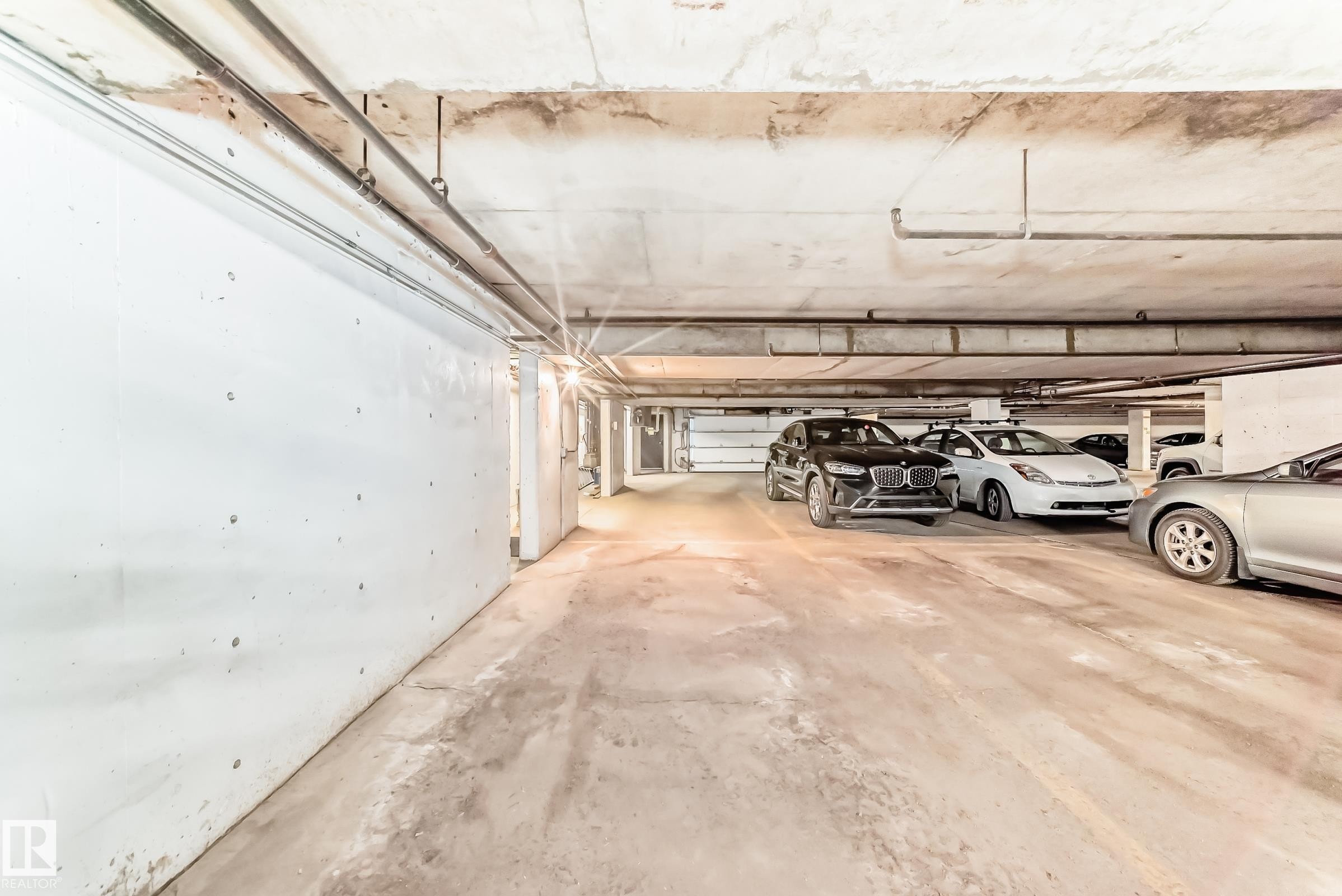 Underground parking area featuring concrete flooring, exposed overhead piping, and a bright light source illuminating the space - 7930 111 Street, Edmonton, AB - Indoor Photo Showing Garage