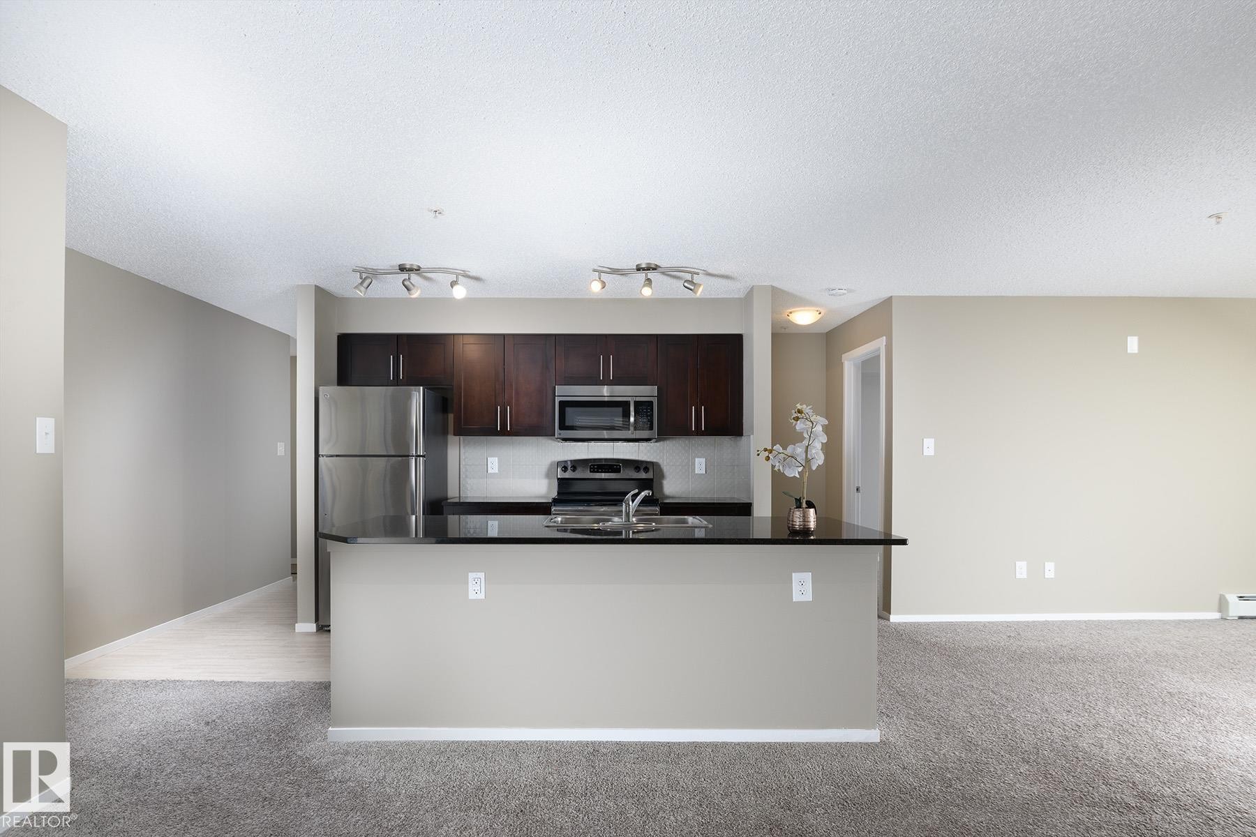 Kitchen featuring dark wood cabinetry, stainless steel appliances, and a black countertop island - 102 25 Element Dr, St. Albert, AB