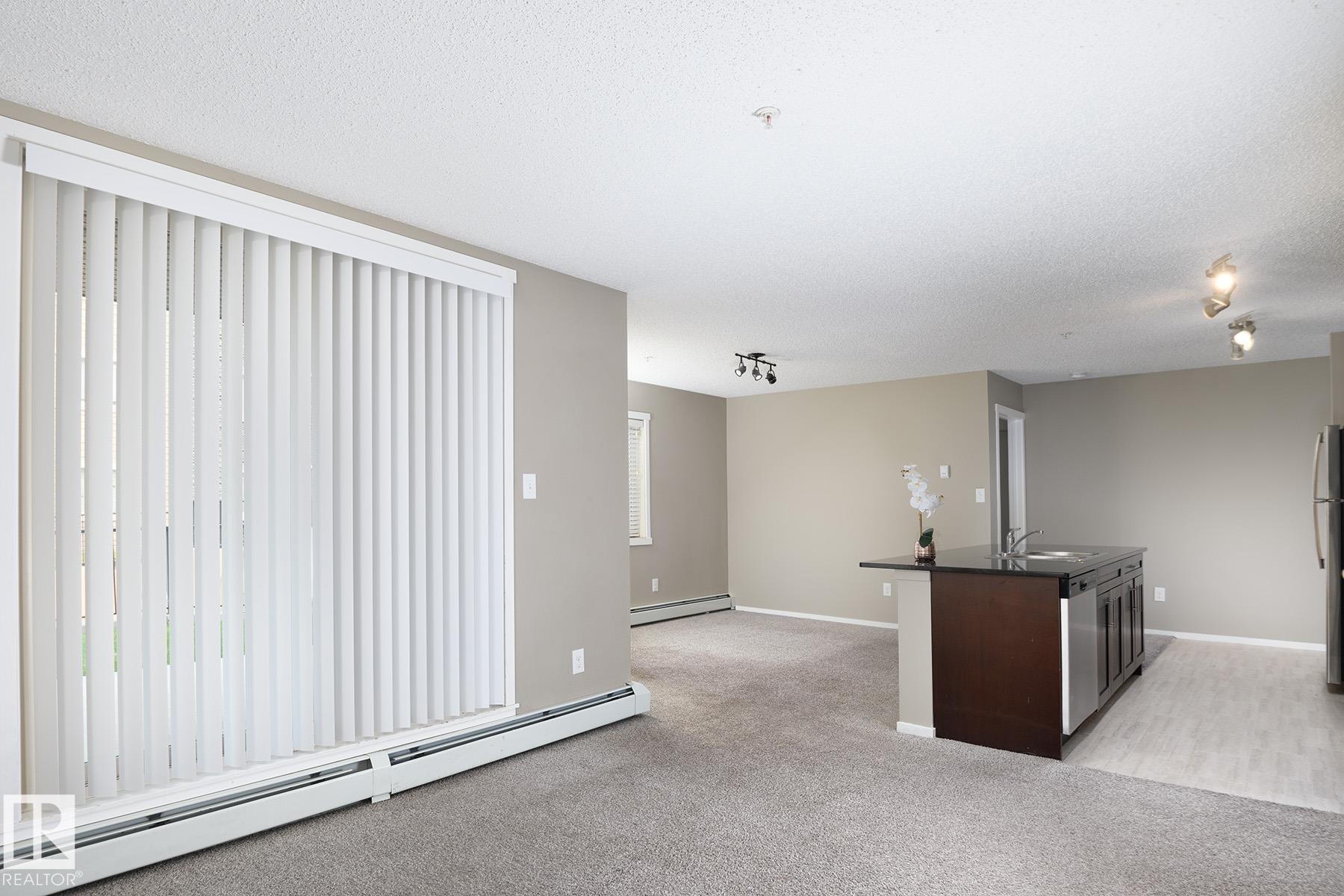 Spacious open-concept living area featuring a kitchen island with sink, stainless steel dishwasher, and dark cabinetry - 102 25 Element Dr, St. Albert, AB