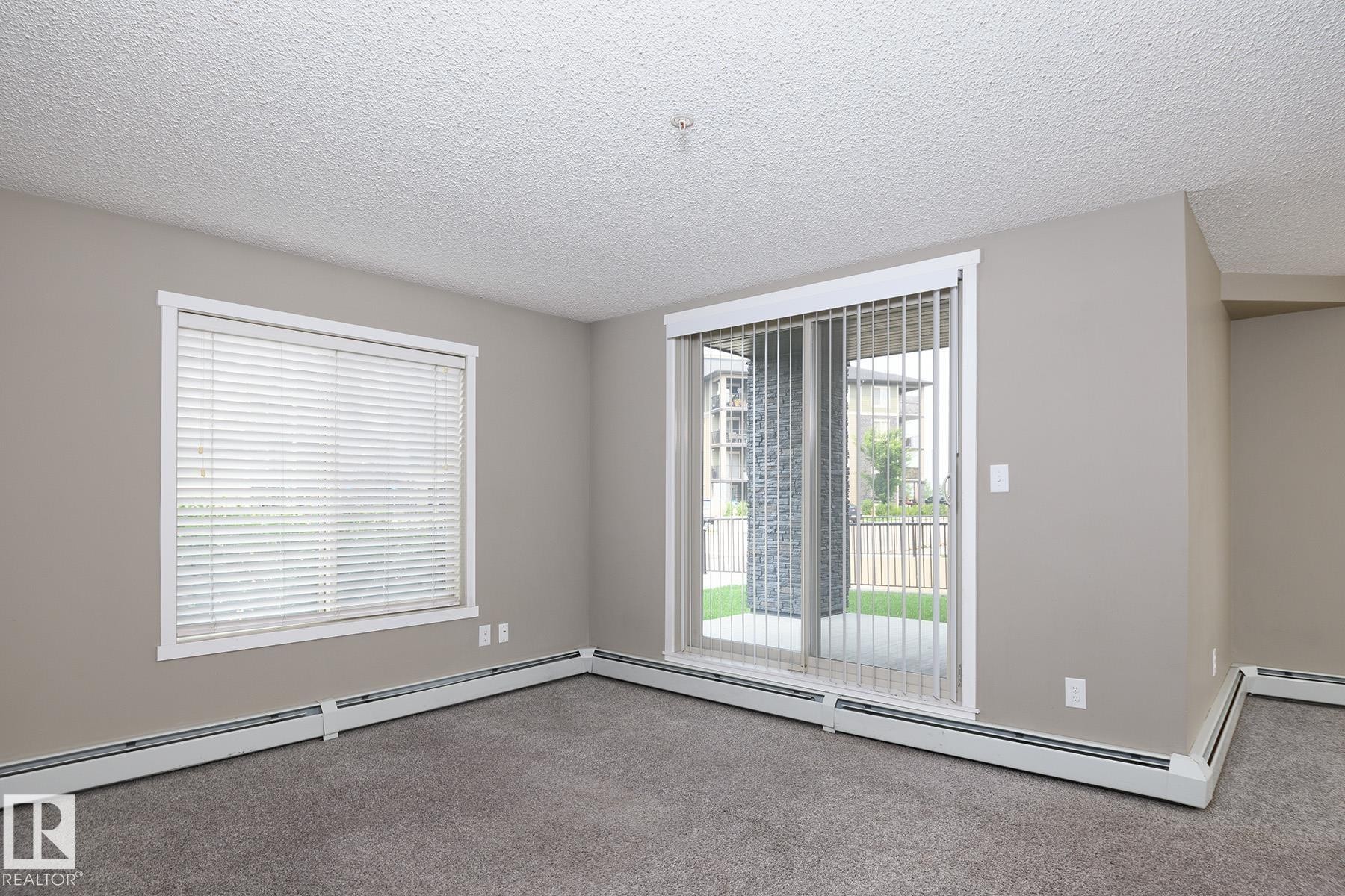 Room featuring neutral-toned walls, gray carpet flooring, and a textured white ceiling - 102 25 Element Dr, St. Albert, AB