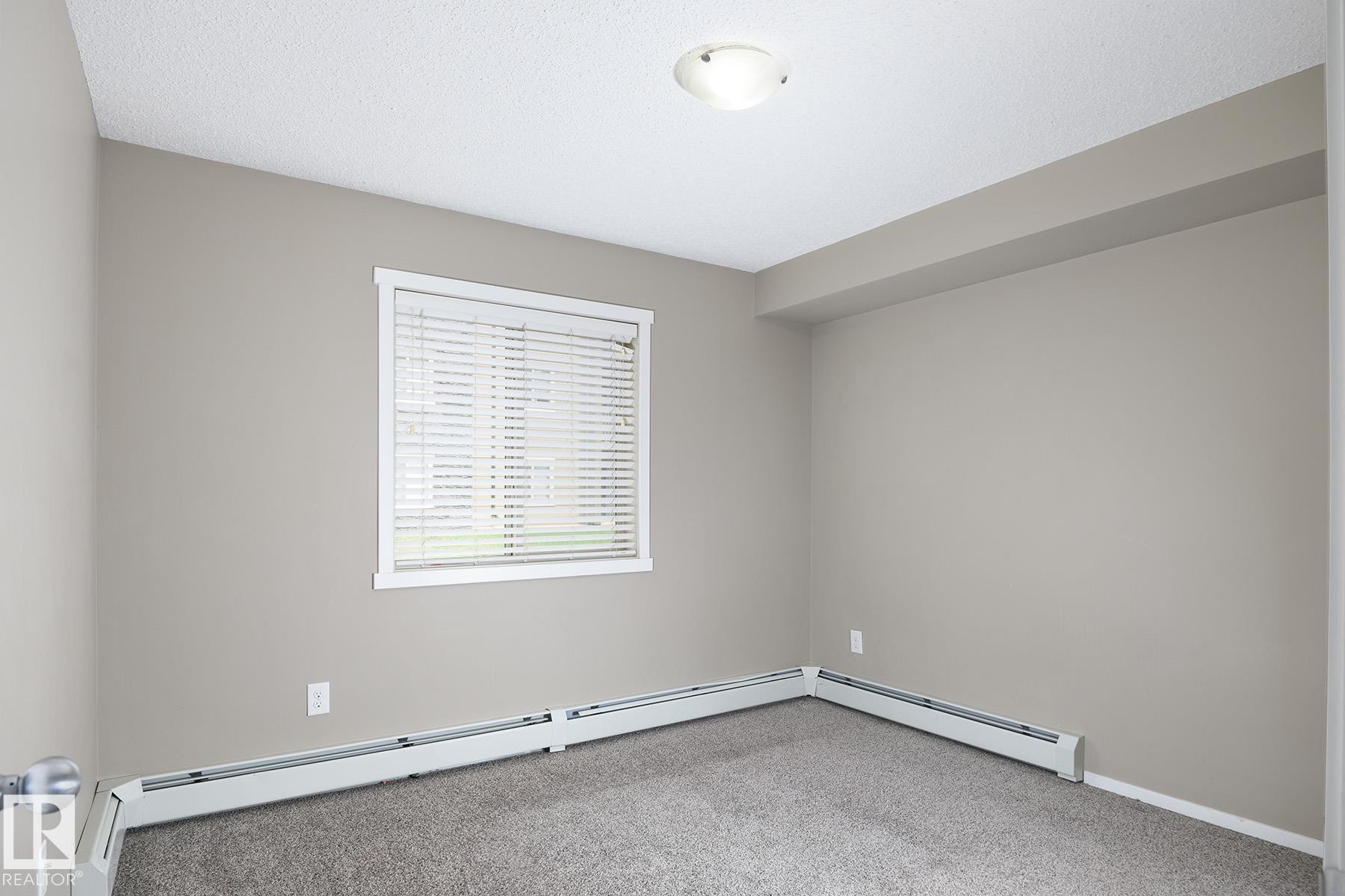 Carpeted room with neutral wall paint and a single window featuring horizontal blinds - 102 25 Element Dr, St. Albert, AB