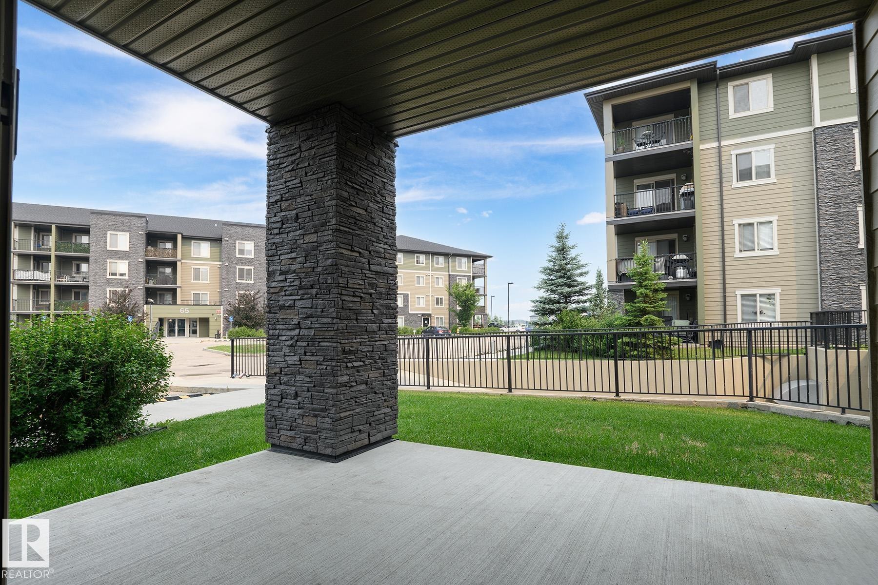 Private concrete patio with a stone-clad pillar, overlooking a landscaped lawn and black metal fencing - 102 25 Element Dr, St. Albert, AB