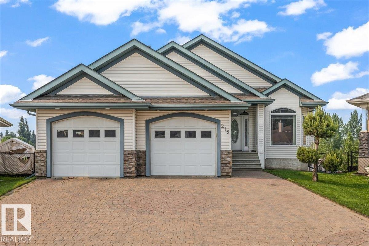 Front exterior featuring a dual-bay garage, stone accents, and an arched entry window - 215 Westerra Point(E), Stony Plain, AB