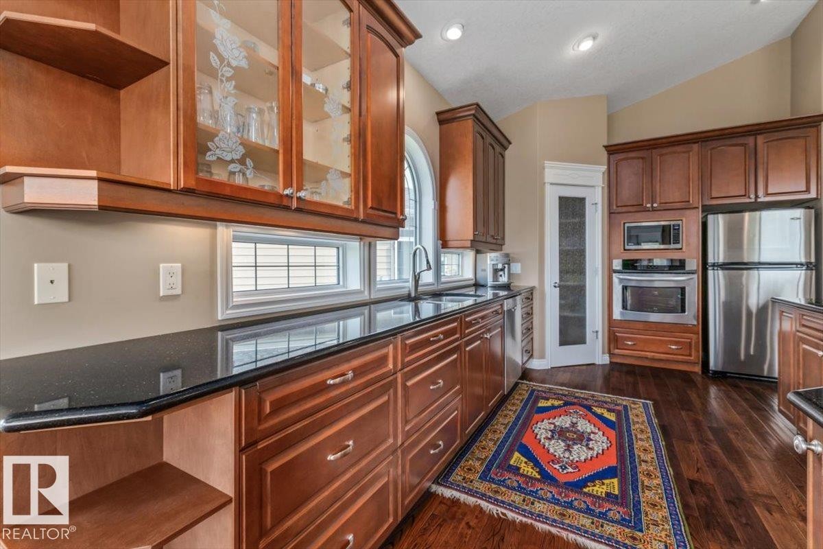 Kitchen featuring rich wood cabinetry, dark countertops, a built-in stainless steel oven and microwave, and an arched window above the sink - 215 Westerra Point(E), Stony Plain, AB