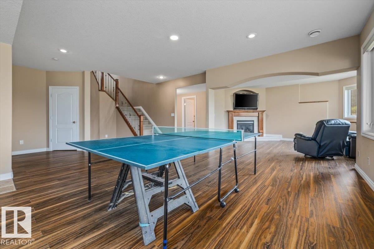 Expansive lower-level space featuring rich wood-finish flooring, recessed lighting, and a prominent staircase with wood and white balusters - 215 Westerra Point(E), Stony Plain, AB