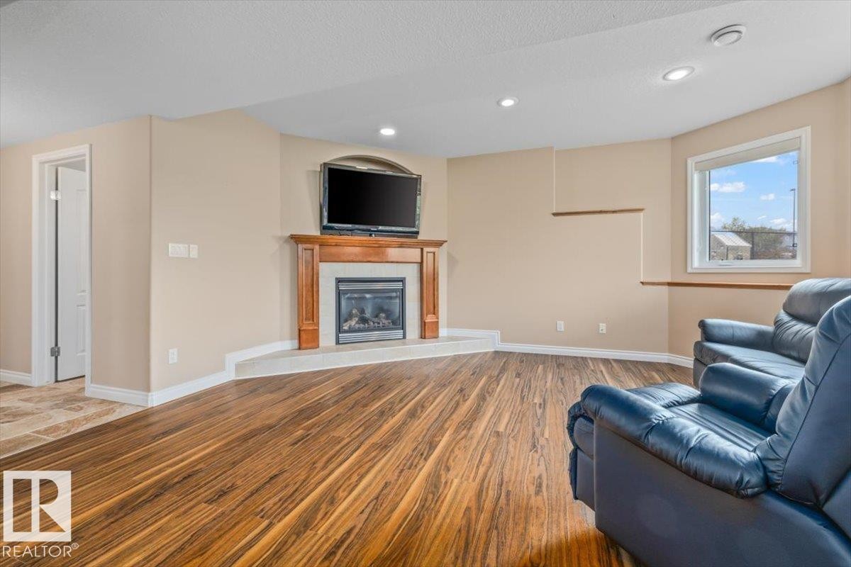 Living area featuring wood-finish flooring, a corner fireplace with a wood mantel, and a large window - 215 Westerra Point(E), Stony Plain, AB