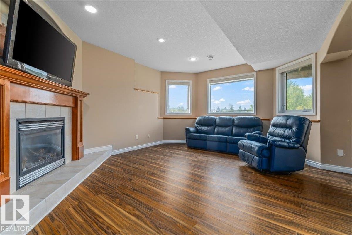 Spacious room featuring wood-finish flooring, a built-in fireplace with a tile surround and wood mantel, recessed lighting, and multiple windows - 215 Westerra Point(E), Stony Plain, AB