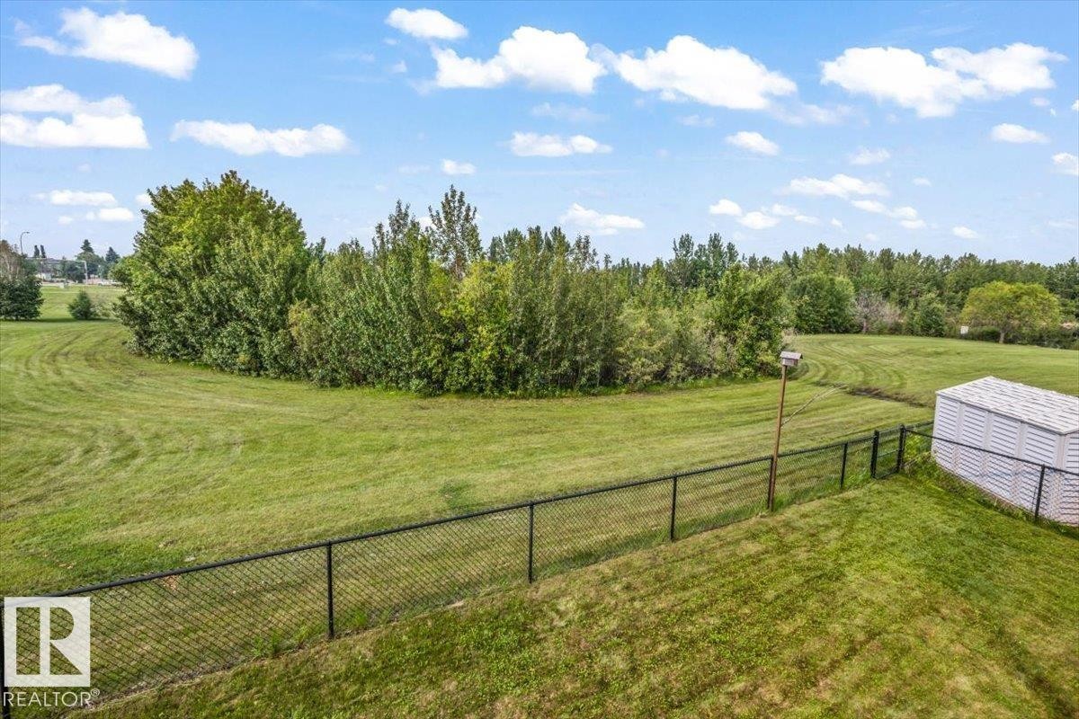 Expansive green space featuring a chain-link fence, mature trees, and a storage shed - 215 Westerra Point(E), Stony Plain, AB