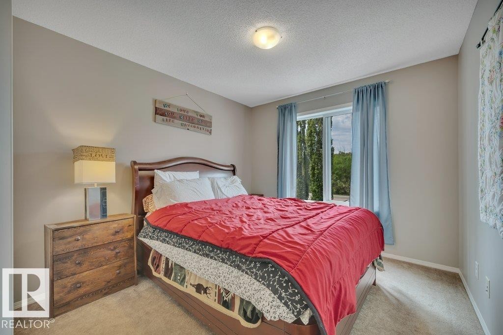 Carpeted bedroom featuring a large window, neutral wall paint, and a ceiling-mounted light fixture - 6042 214 Street, Edmonton, AB - Indoor Photo Showing Bedroom