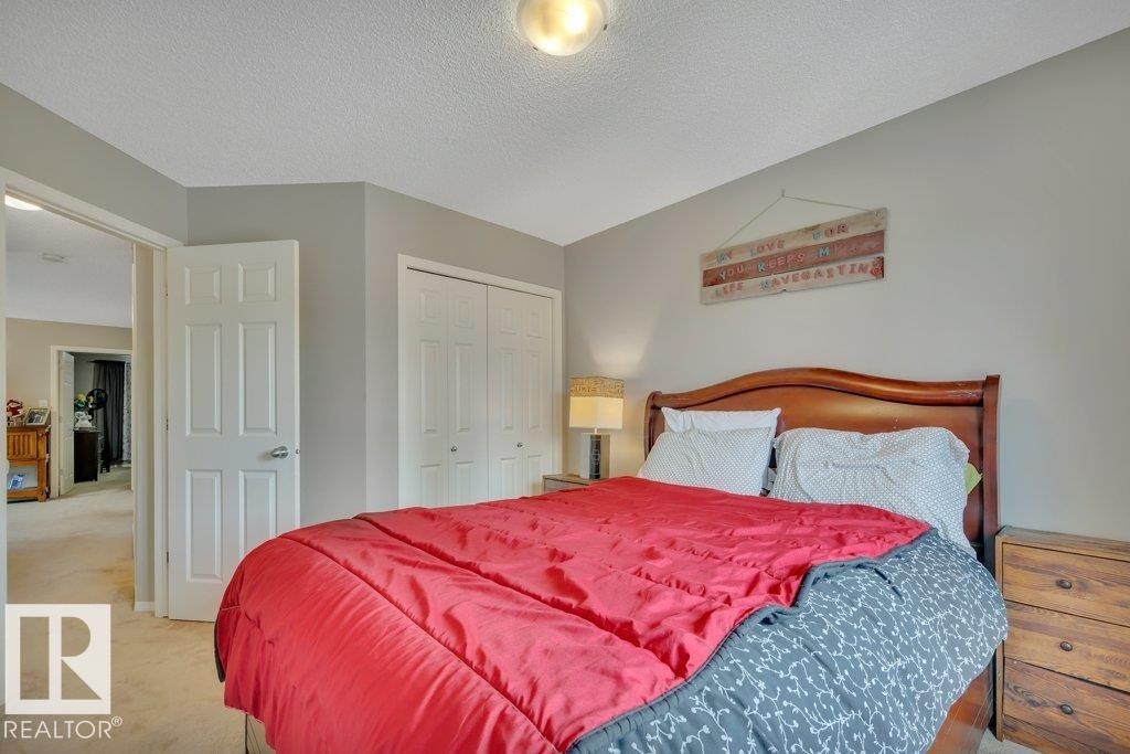 Bedroom featuring neutral-toned walls, white bi-fold closet doors, a white paneled door, textured ceiling, and light-colored carpet flooring - 6042 214 Street, Edmonton, AB - Indoor Photo Showing Bedroom