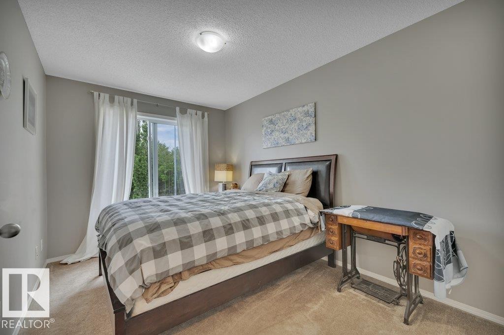Spacious room featuring carpet flooring, neutral wall paint, and a large window with white curtain panels - 6042 214 Street, Edmonton, AB - Indoor Photo Showing Bedroom