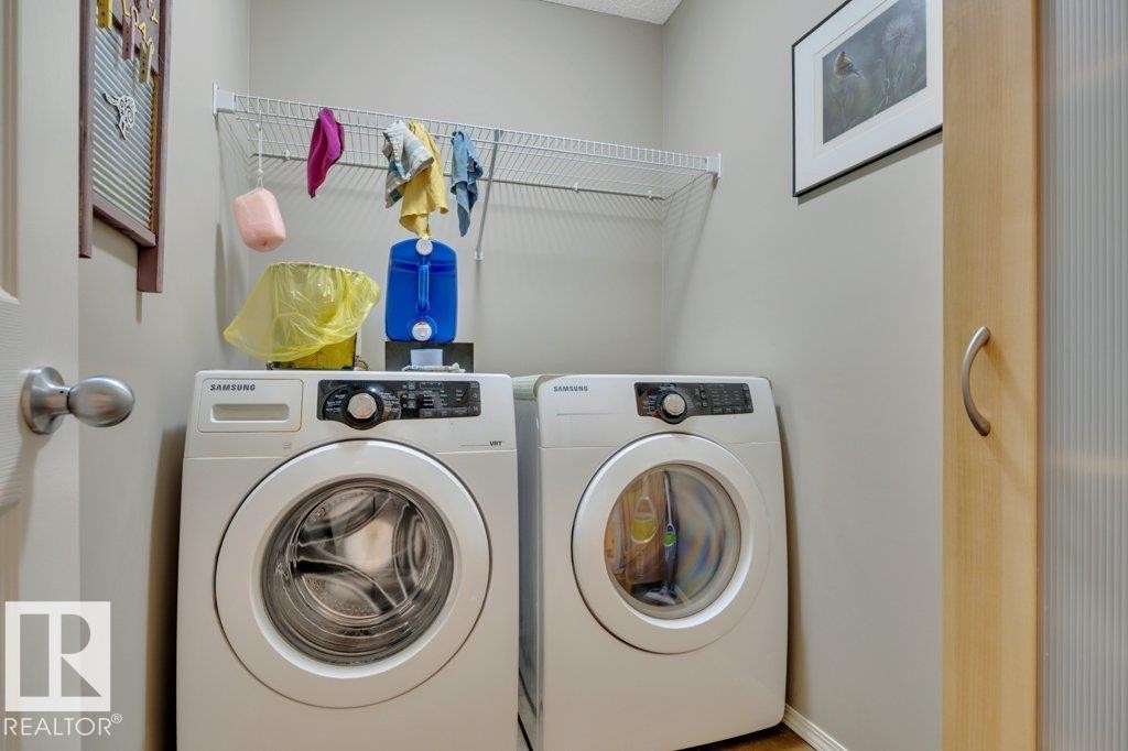 Dedicated upper level laundry area featuring a white front-loading washer and dryer, an overhead wire shelving unit, and warm wood-finish flooring - 6042 214 Street, Edmonton, AB - Indoor Photo Showing Laundry Room