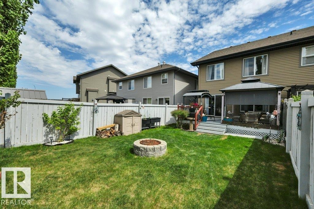 Expansive backyard featuring a stone-look fire pit, green lawn, full privacy fencing, and a deck - 6042 214 Street, Edmonton, AB - Outdoor With Deck Patio Veranda