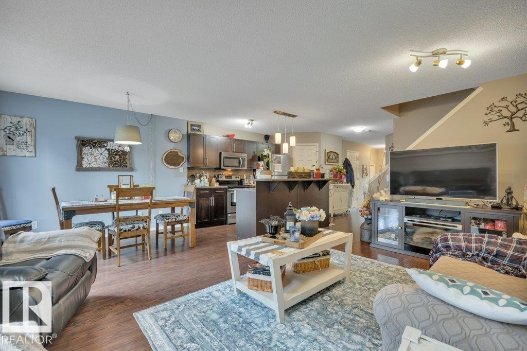 Open-concept living space, a kitchen with dark cabinetry and stainless steel appliances, and a dining area with a pendant light fixture - 6042 214 Street, Edmonton, AB - Indoor Photo Showing Living Room