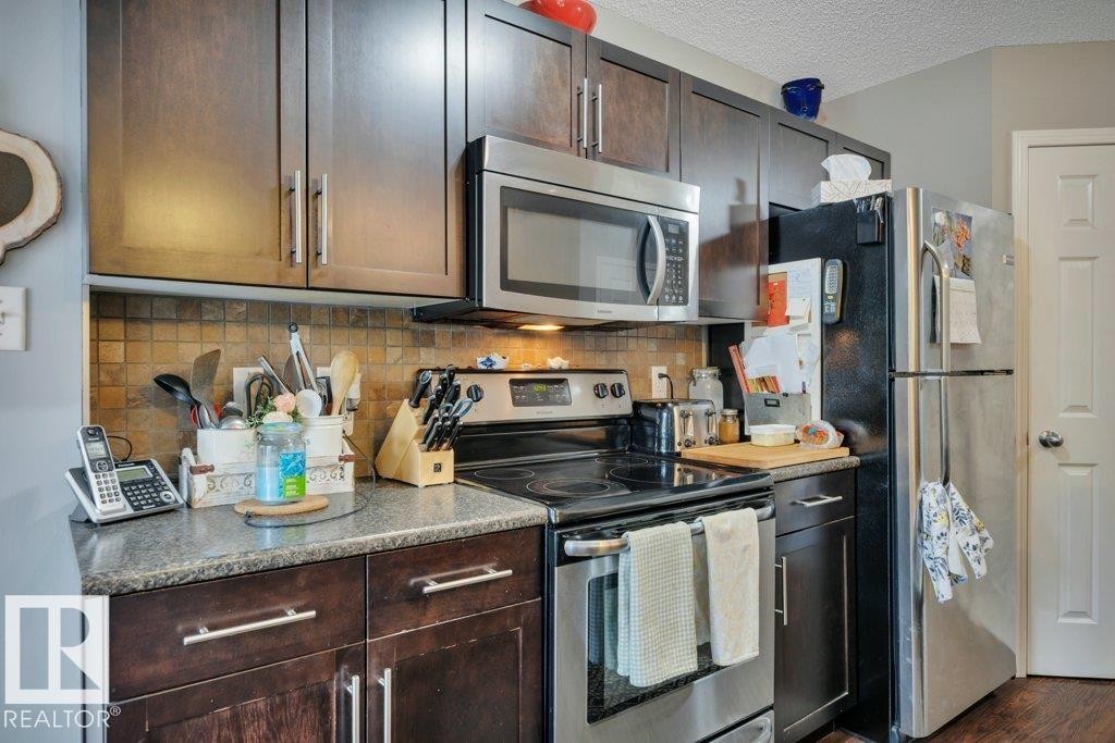 Kitchen featuring dark wood-finish cabinetry with brushed nickel hardware, stainless steel appliances, a tile backsplash. - 6042 214 Street, Edmonton, AB - Indoor Photo Showing Kitchen