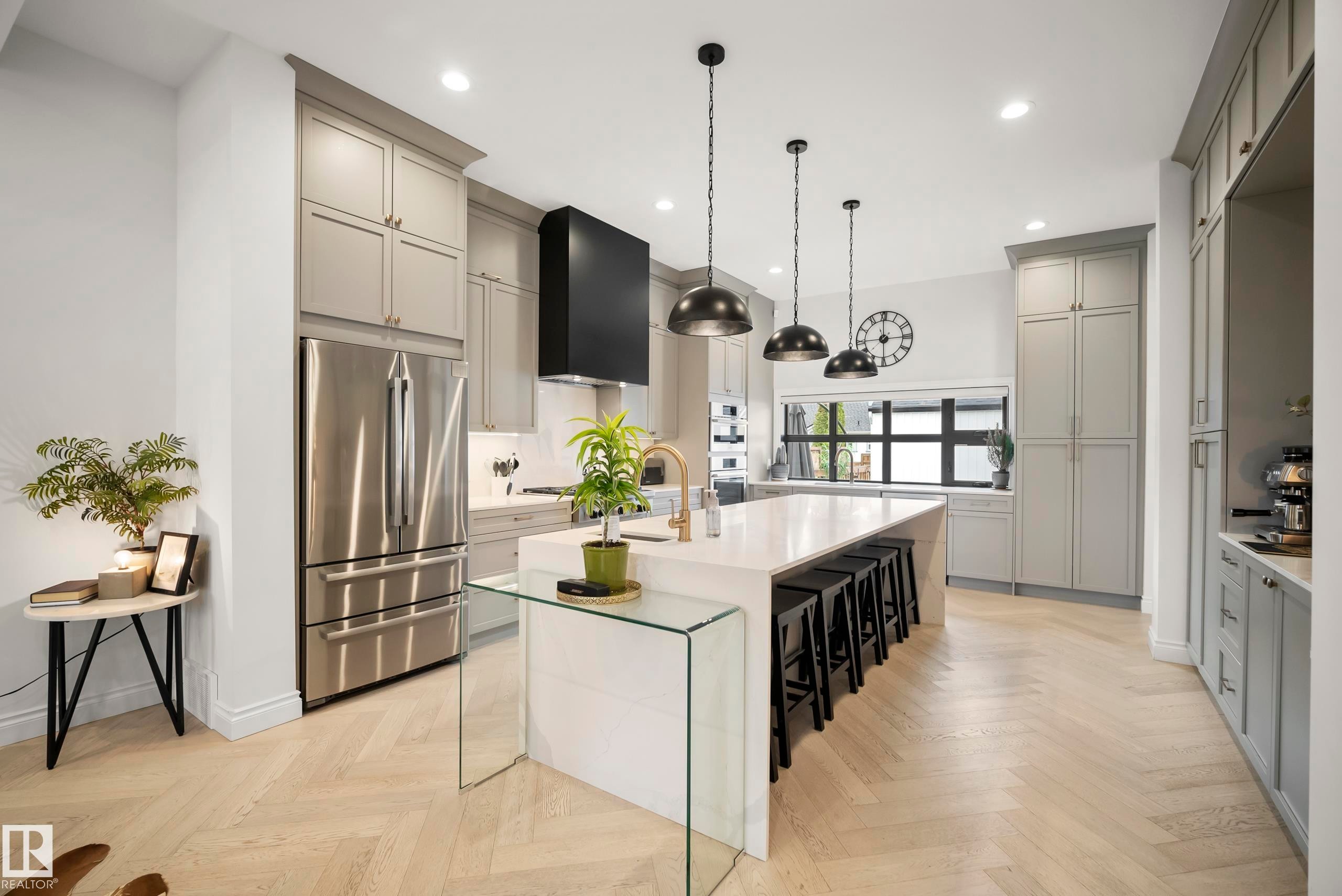 Contemporary kitchen featuring light gray cabinetry, stainless steel appliances, a large center island with seating, pendant lighting, and light wood-finish flooring in a herringbone pattern - 6115 111 Avenue, Edmonton, AB - Indoor Photo Showing Kitchen With Upgraded Kitchen