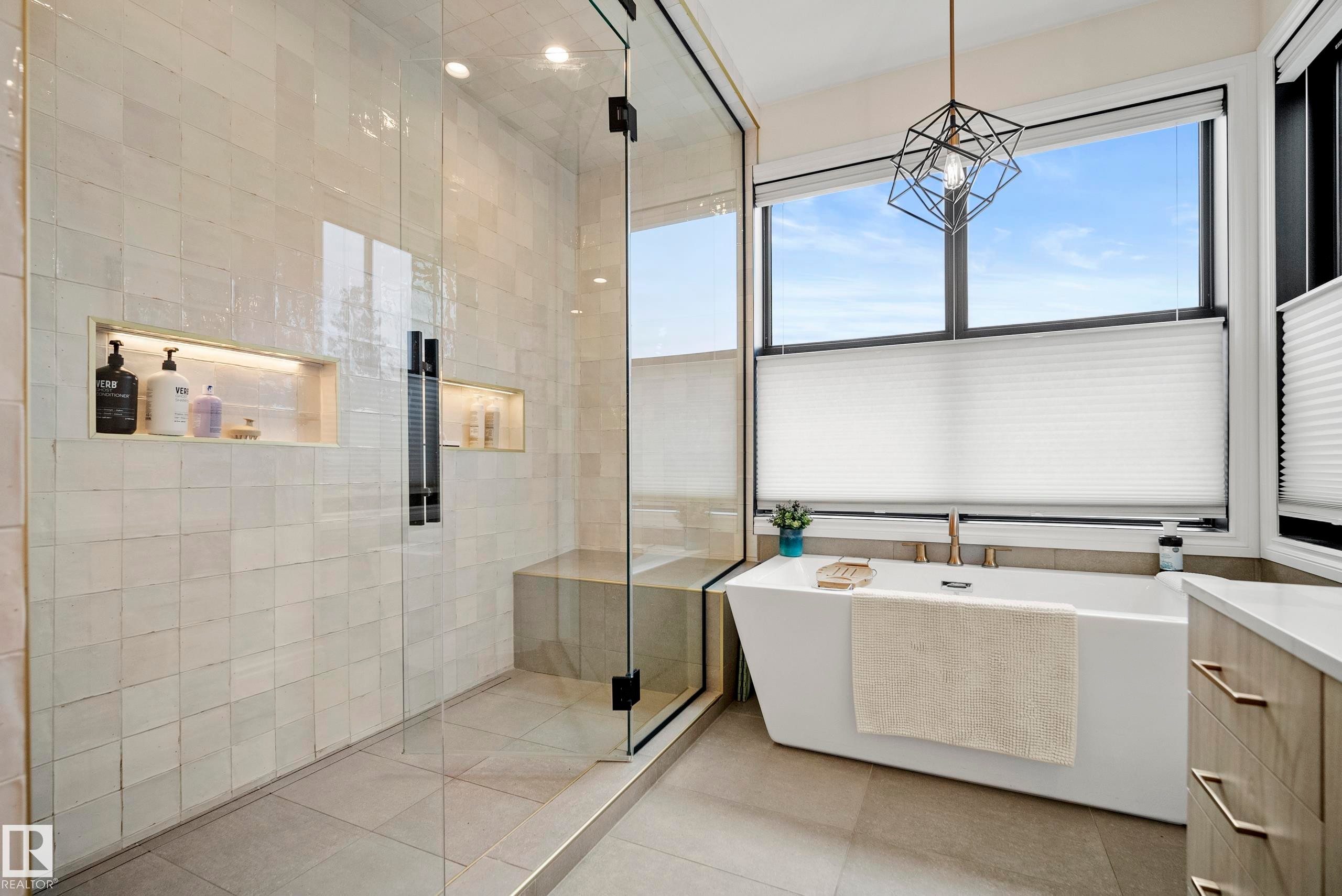 Modern bathroom featuring a freestanding tub with a brass-finish faucet, a geometric pendant light, and large windows with blinds - 6115 111 Avenue, Edmonton, AB - Indoor Photo Showing Bathroom