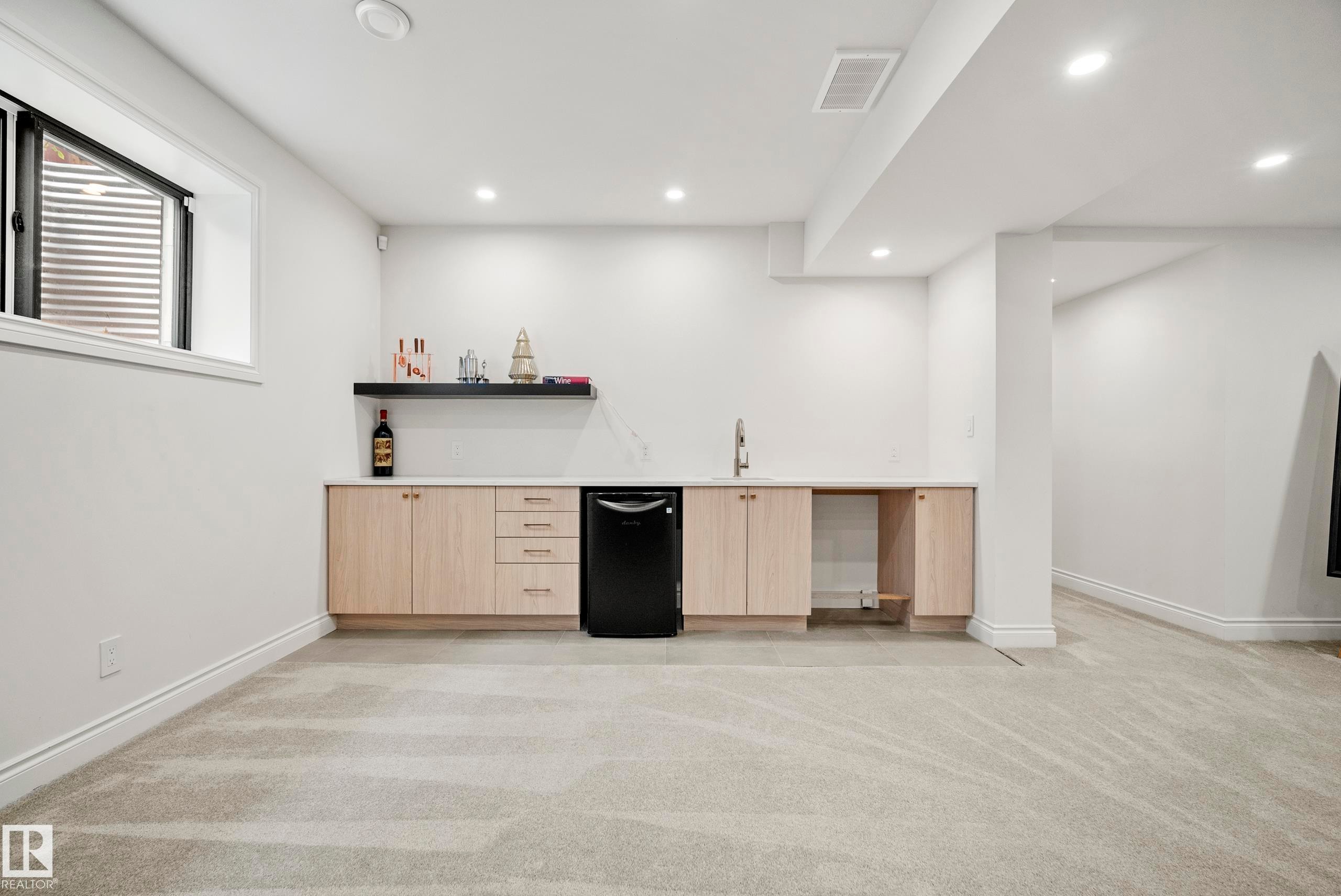 Lower-level entertainment space featuring a wet bar with light wood-finish cabinetry, a black beverage refrigerator, and a white countertop - 6115 111 Avenue, Edmonton, AB - Indoor