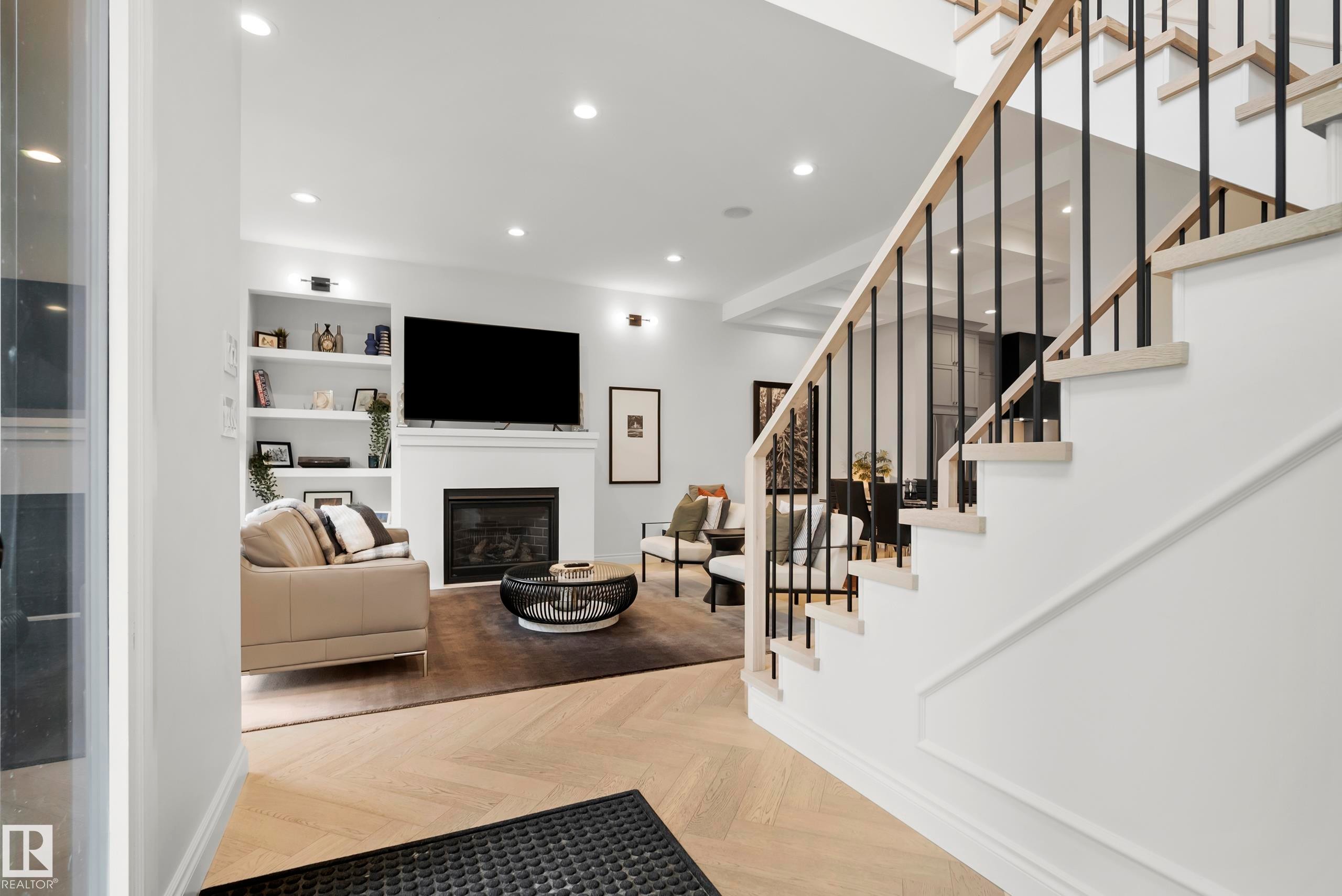 Herringbone wood-finish flooring extending into a living area featuring a fireplace with a white mantel, built-in shelving, and recessed lighting - 6115 111 Avenue, Edmonton, AB - Indoor Photo Showing Other Room With Fireplace