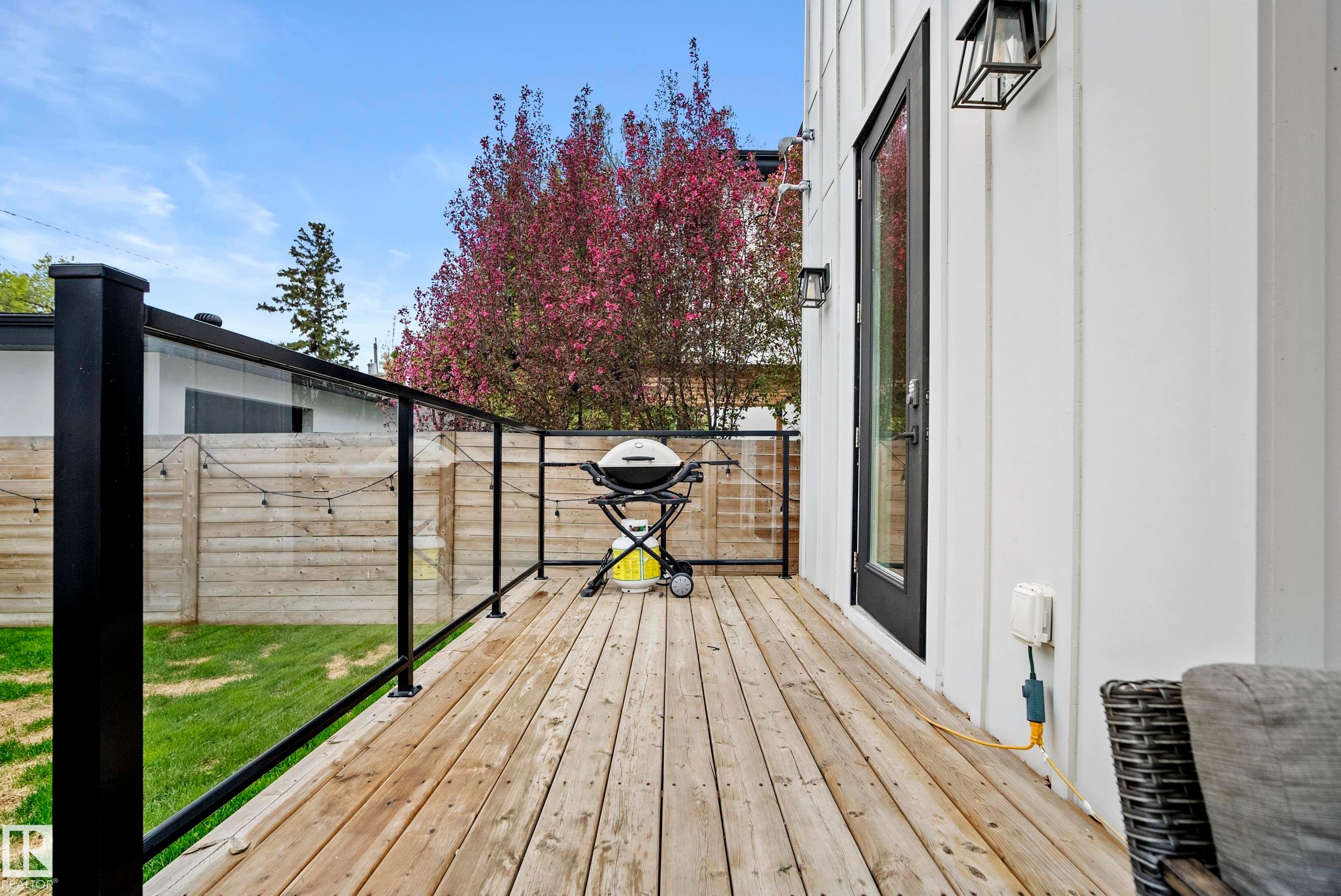 Outdoor deck with natural wood-finish flooring, glass panel railing, and black metal posts - 6115 111 Avenue, Edmonton, AB - Outdoor With Deck Patio Veranda With Exterior