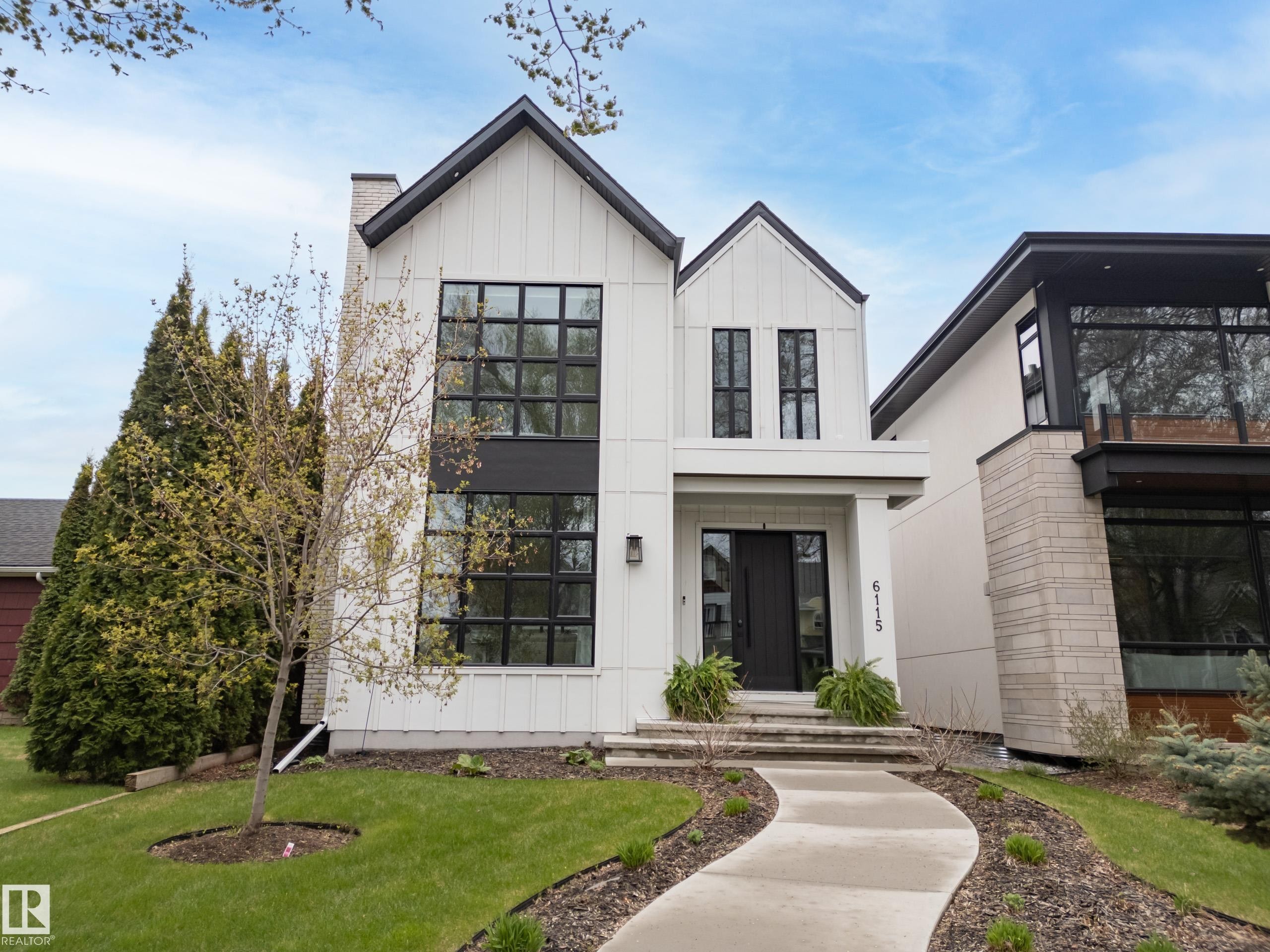 Modern exterior featuring white vertical siding, black-framed windows, a prominent gable roofline, and a curved concrete walkway - 6115 111 Avenue, Edmonton, AB - Outdoor