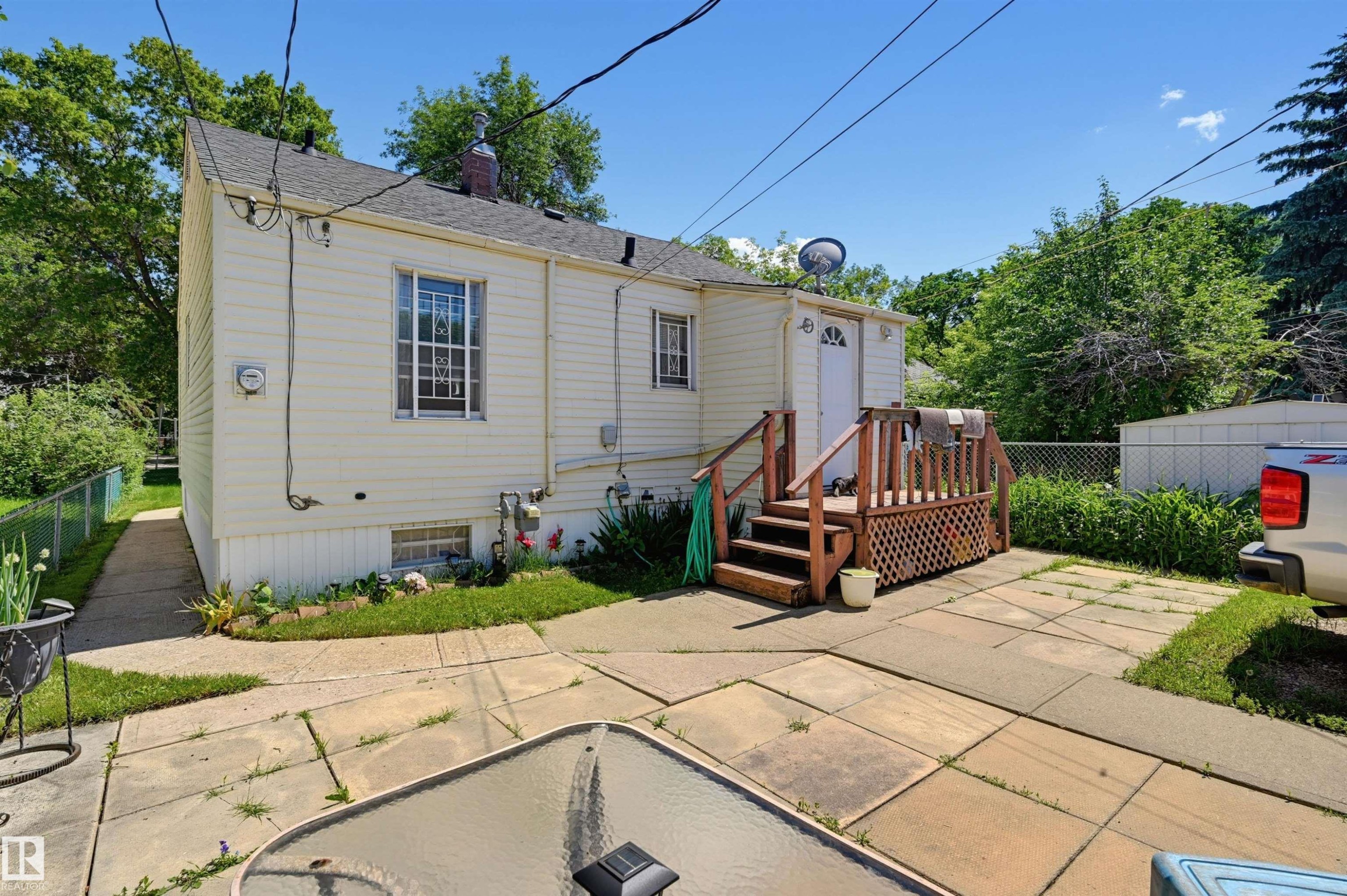 Rear exterior featuring light-colored siding and a wooden deck with lattice detailing - 11414 88 Street Nw, Edmonton, AB