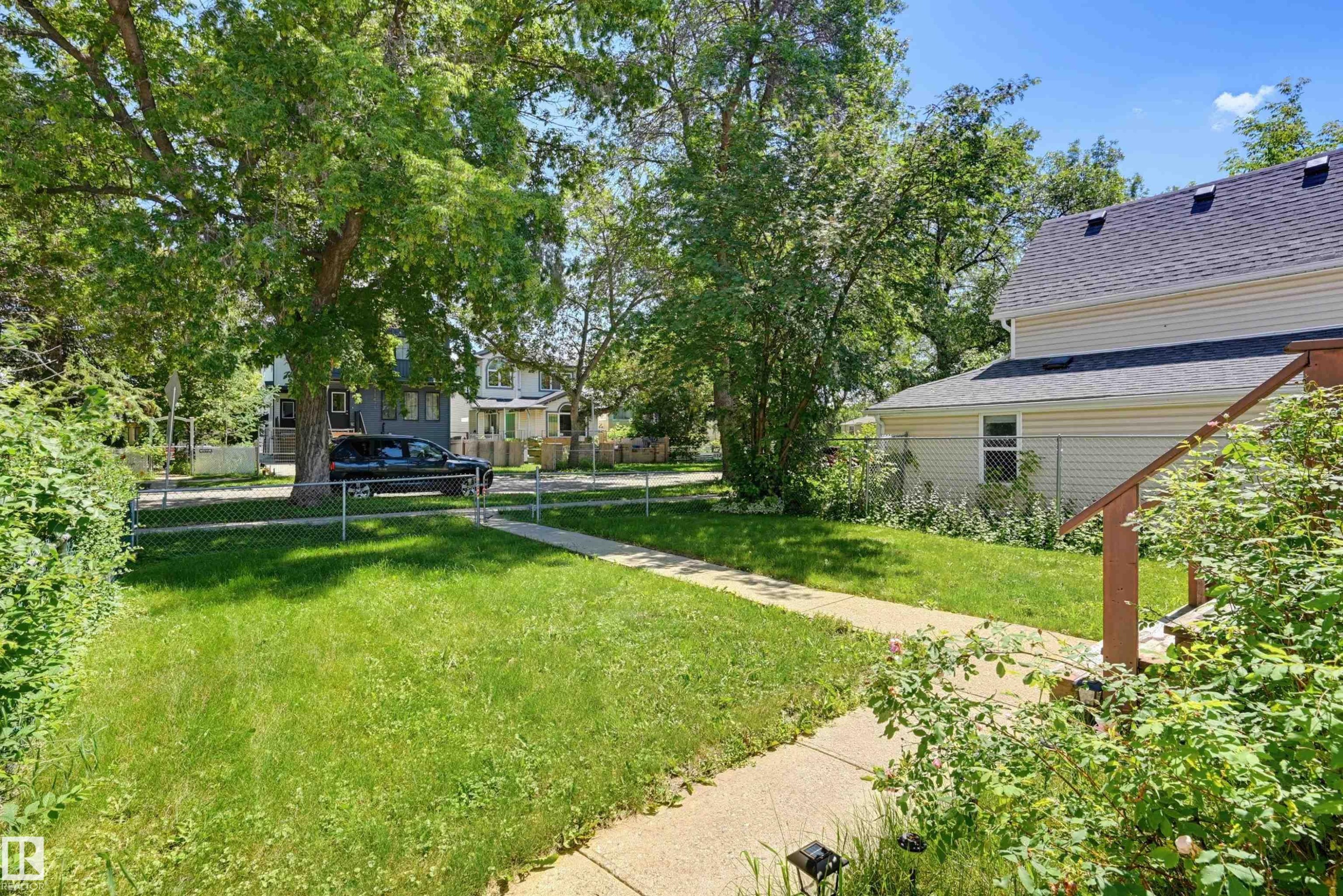 Side yard featuring a concrete walkway, mature trees, and chain-link fencing - 11414 88 Street Nw, Edmonton, AB