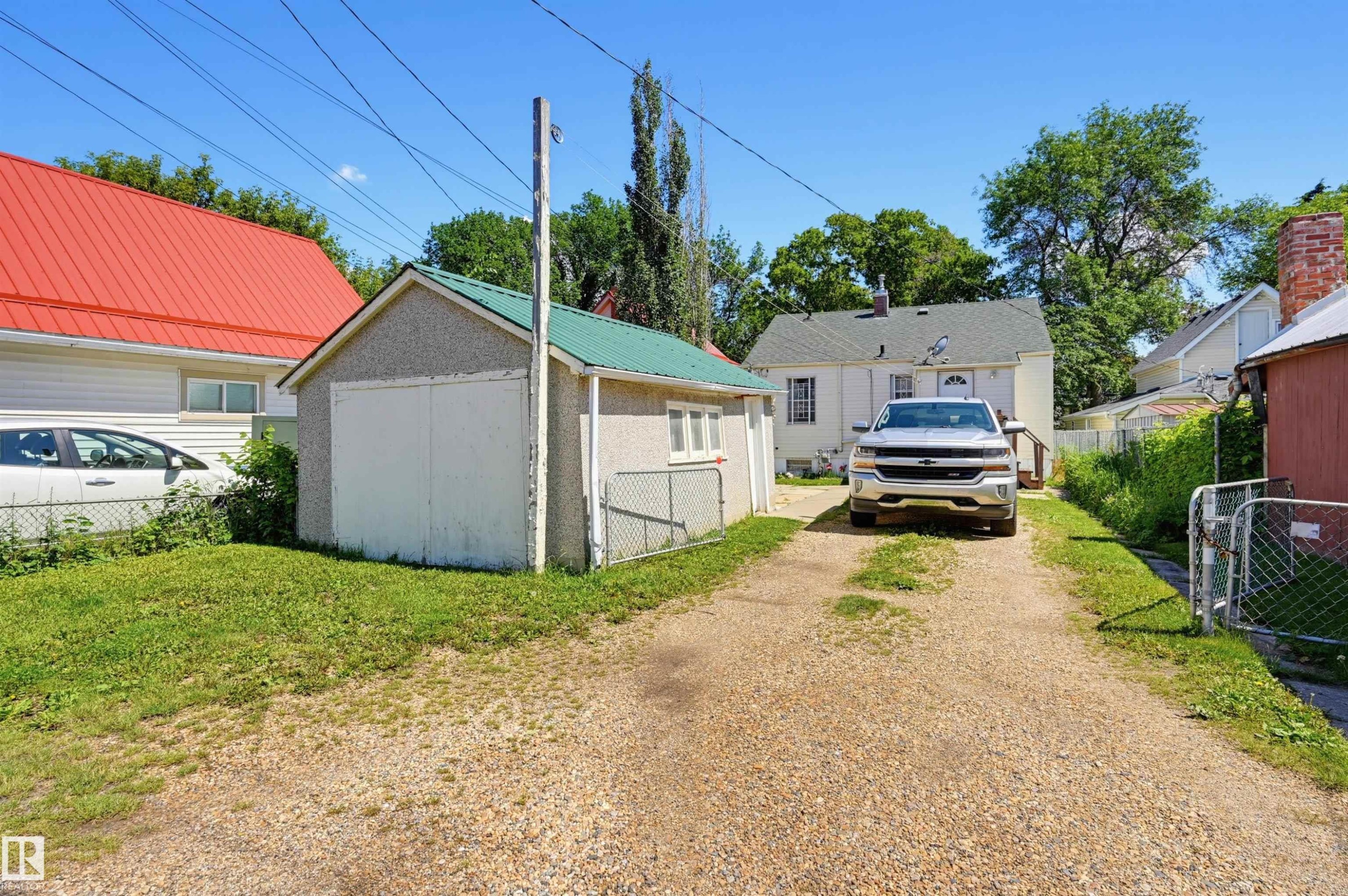 Gravel driveway providing access to a detached garage with a green metal roof and a white overhead door - 11414 88 Street Nw, Edmonton, AB