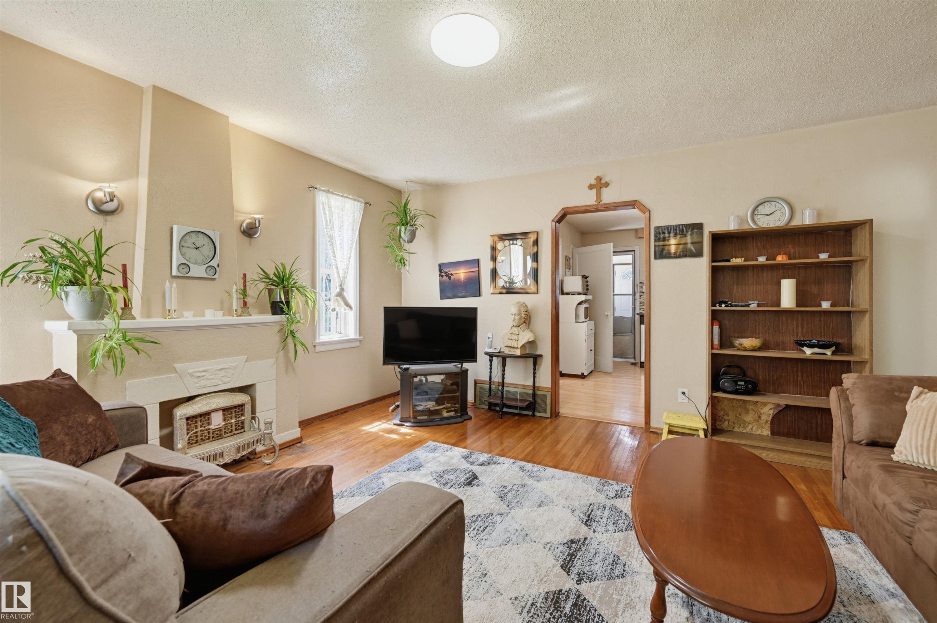 Living area featuring wood-finish flooring, a decorative fireplace with a mantel, recessed wall sconces, and a built-in shelving unit - 11414 88 Street Nw, Edmonton, AB